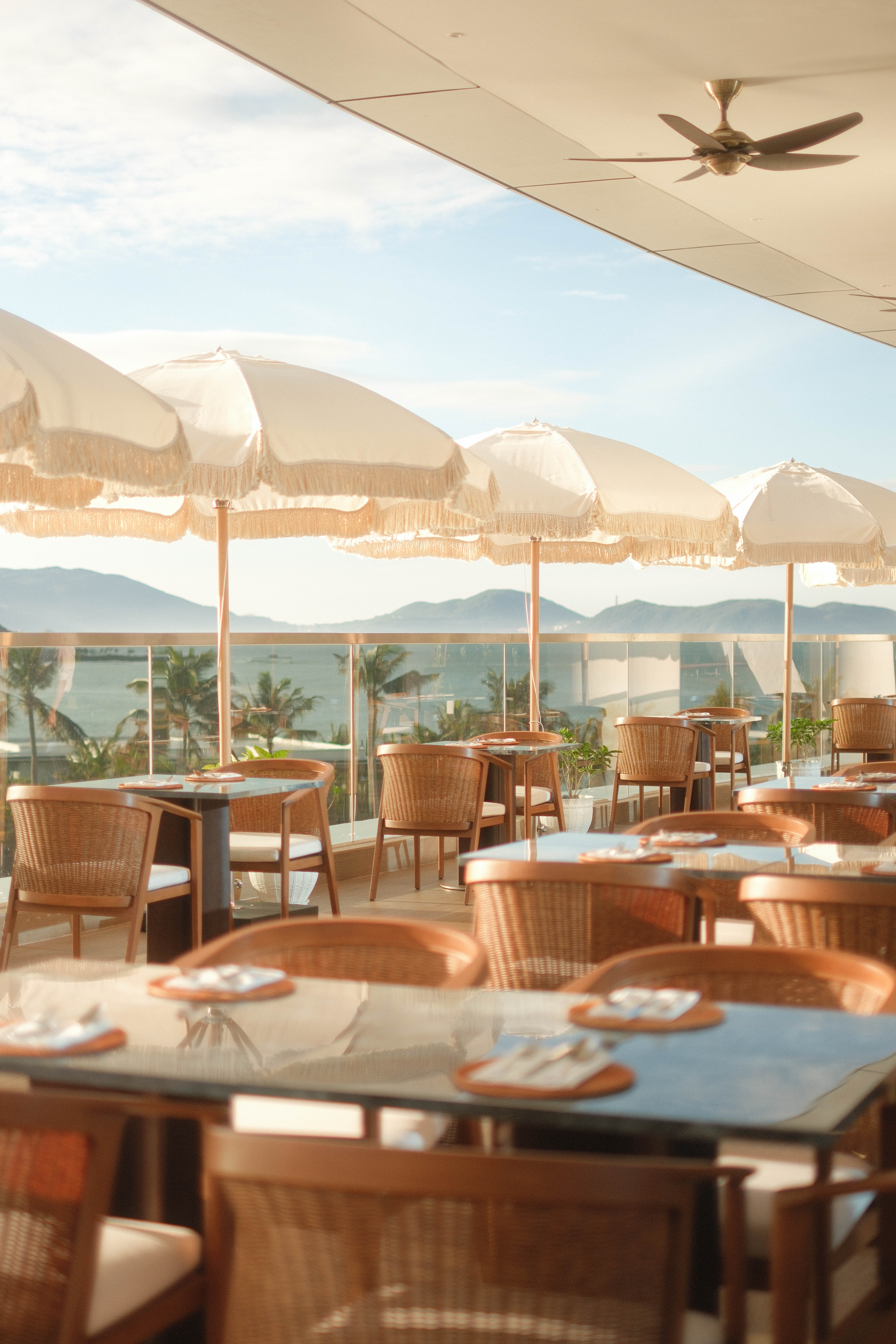 Oceanfront dining patio with white fringed umbrellas and rattan furniture.