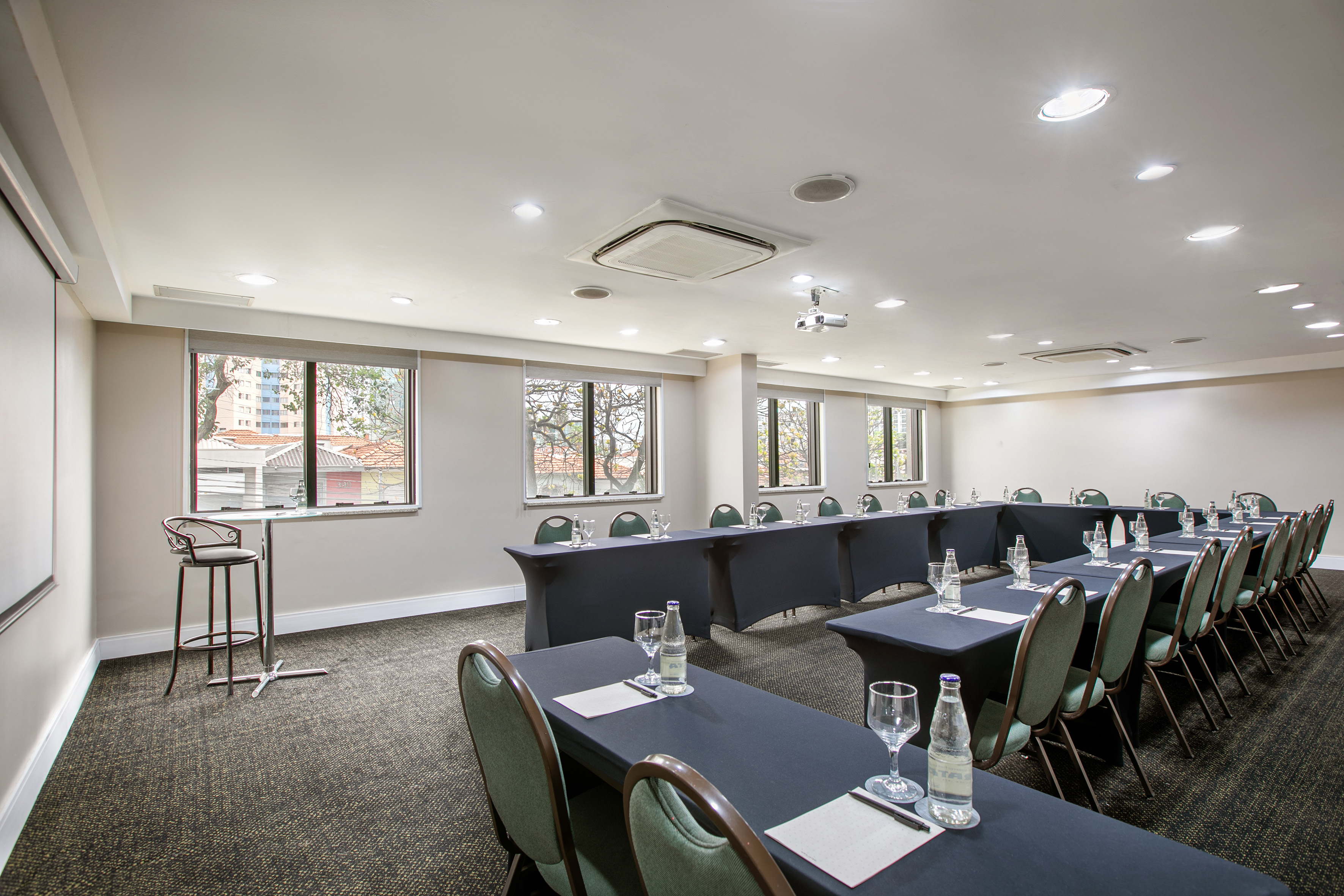 Modern meeting room with U-shaped table setup, projector, and windows.