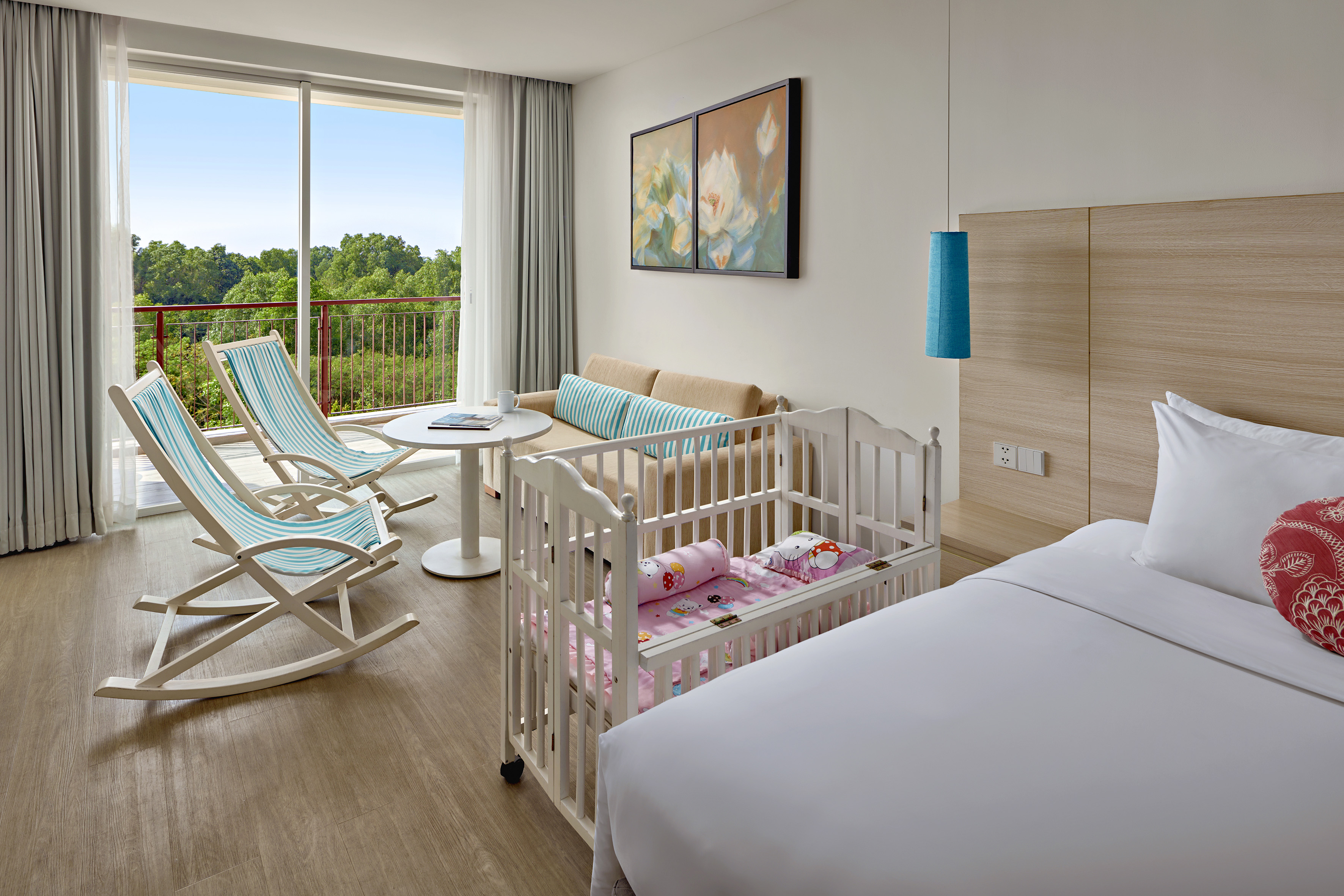 Hotel room with baby crib, balcony, tropical forest view, bed, and sofa.