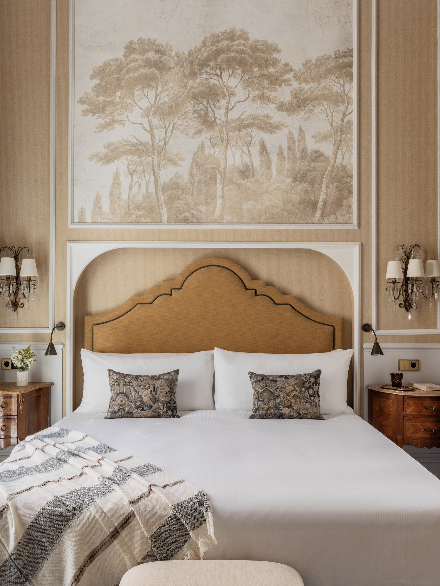 Luxury hotel bedroom with tree mural, upholstered headboard, and ornate patterned curtains.