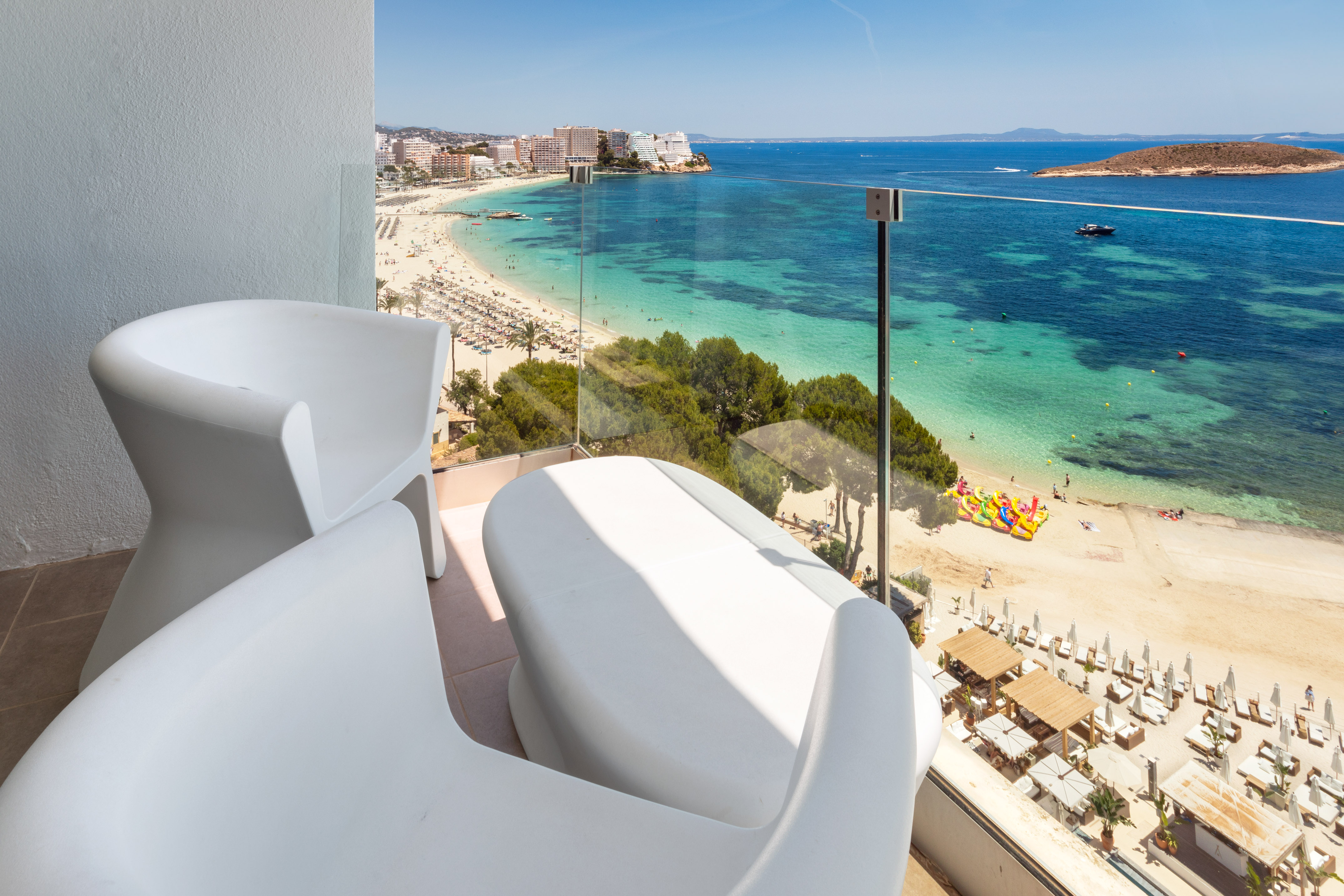 Modern chairs on balcony overlooking sunny beach and turquoise sea.