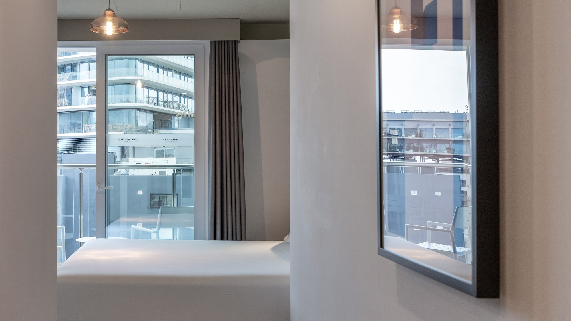 Modern bedroom with white bed, balcony city view, and contemporary lighting.