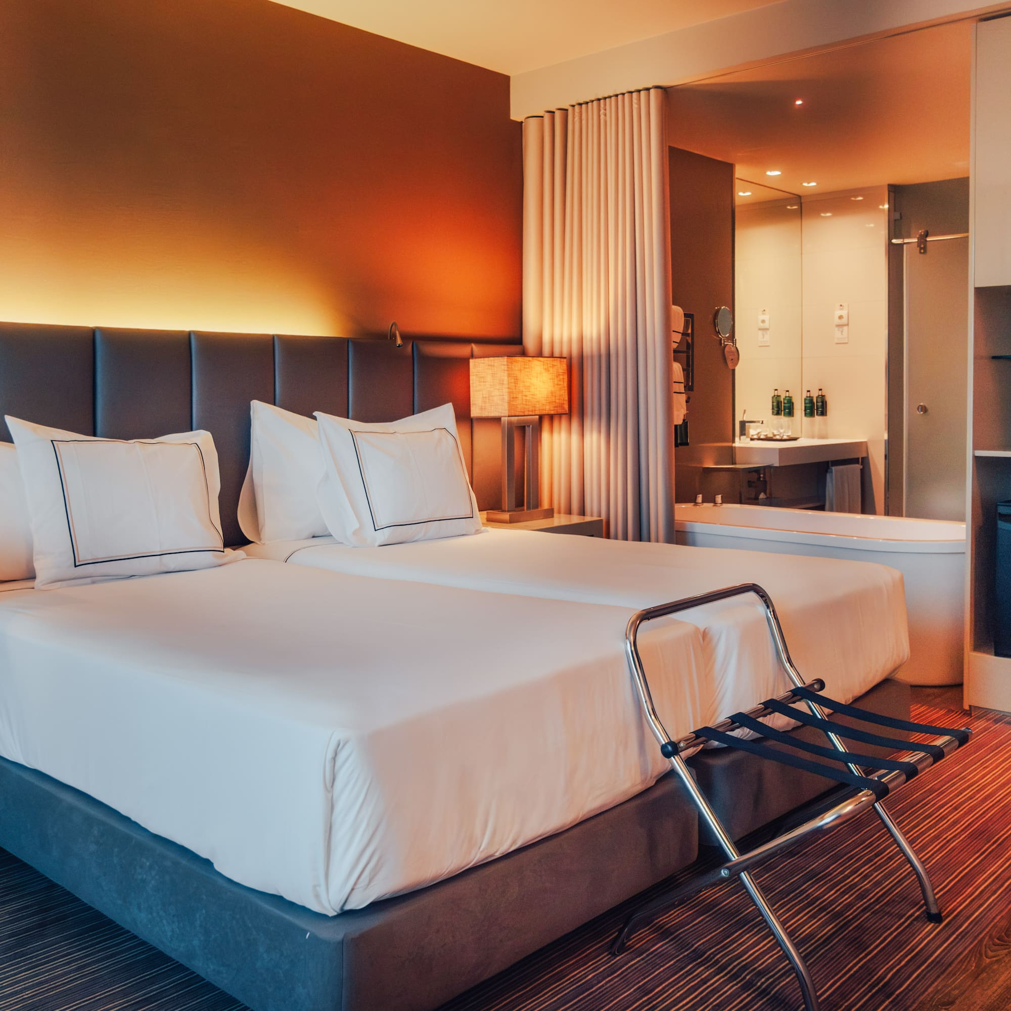 Modern hotel room with twin beds, warm lighting, and open-plan bathroom.