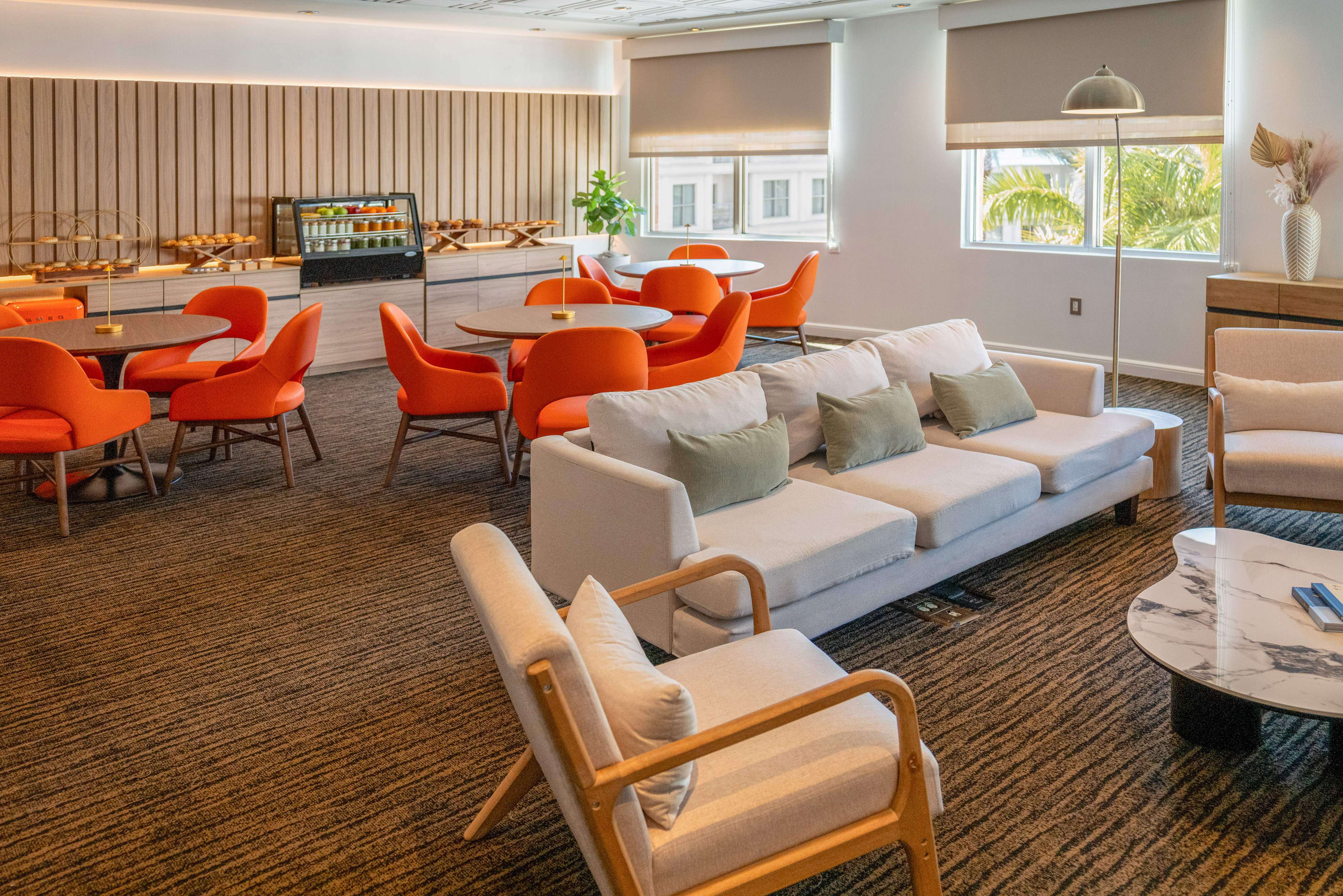 Bright, modern lounge with orange seating, buffet, and natural light from windows.