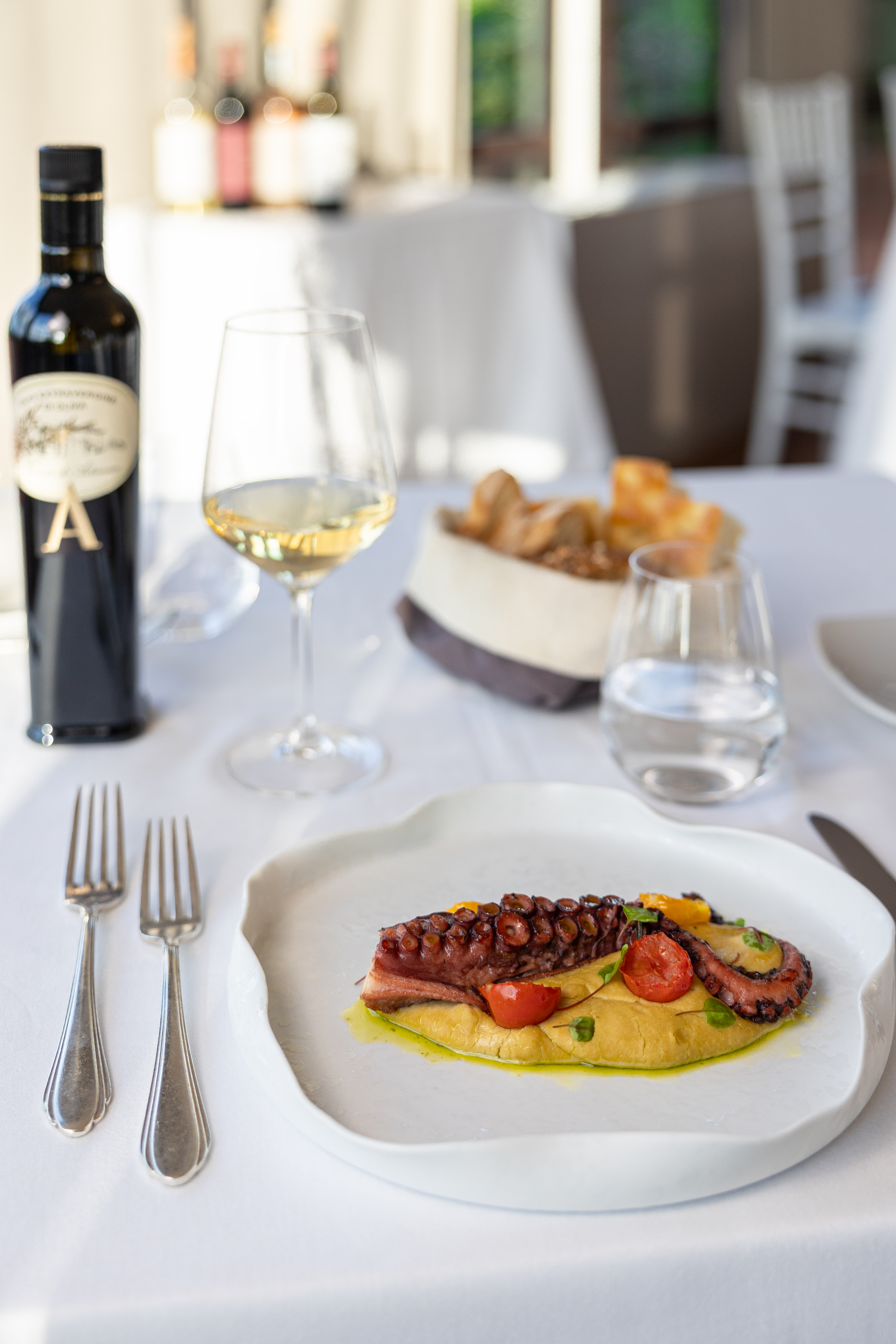 Grilled octopus with yellow puree, cherry tomatoes, wine, and bread on a table.