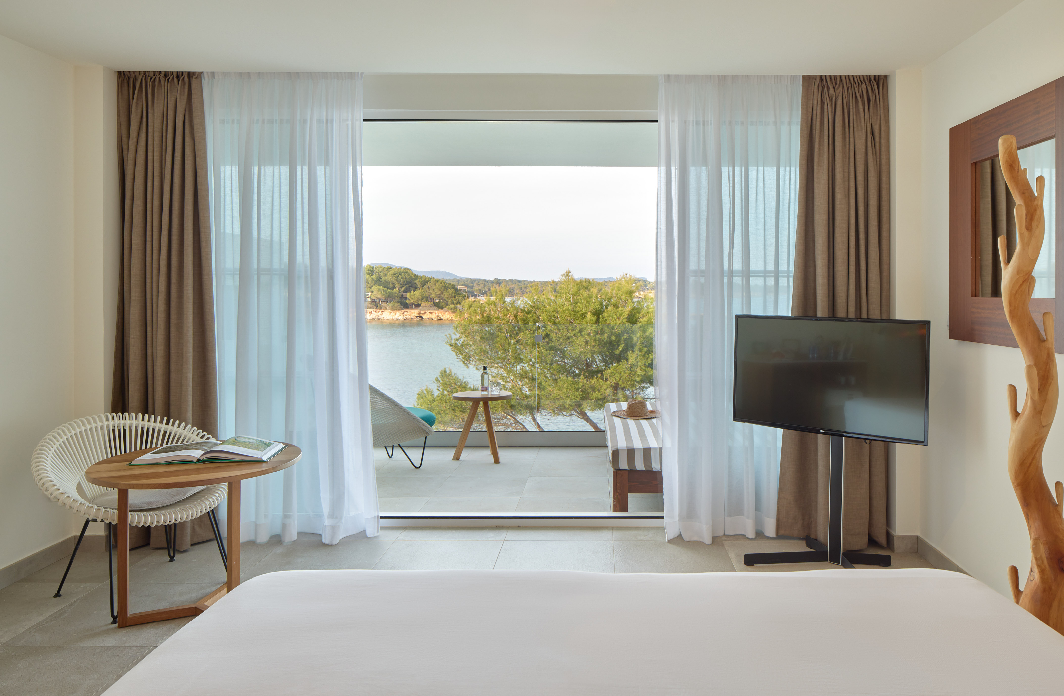 Modern bedroom with sea view balcony, white bed, TV, and outdoor seating.