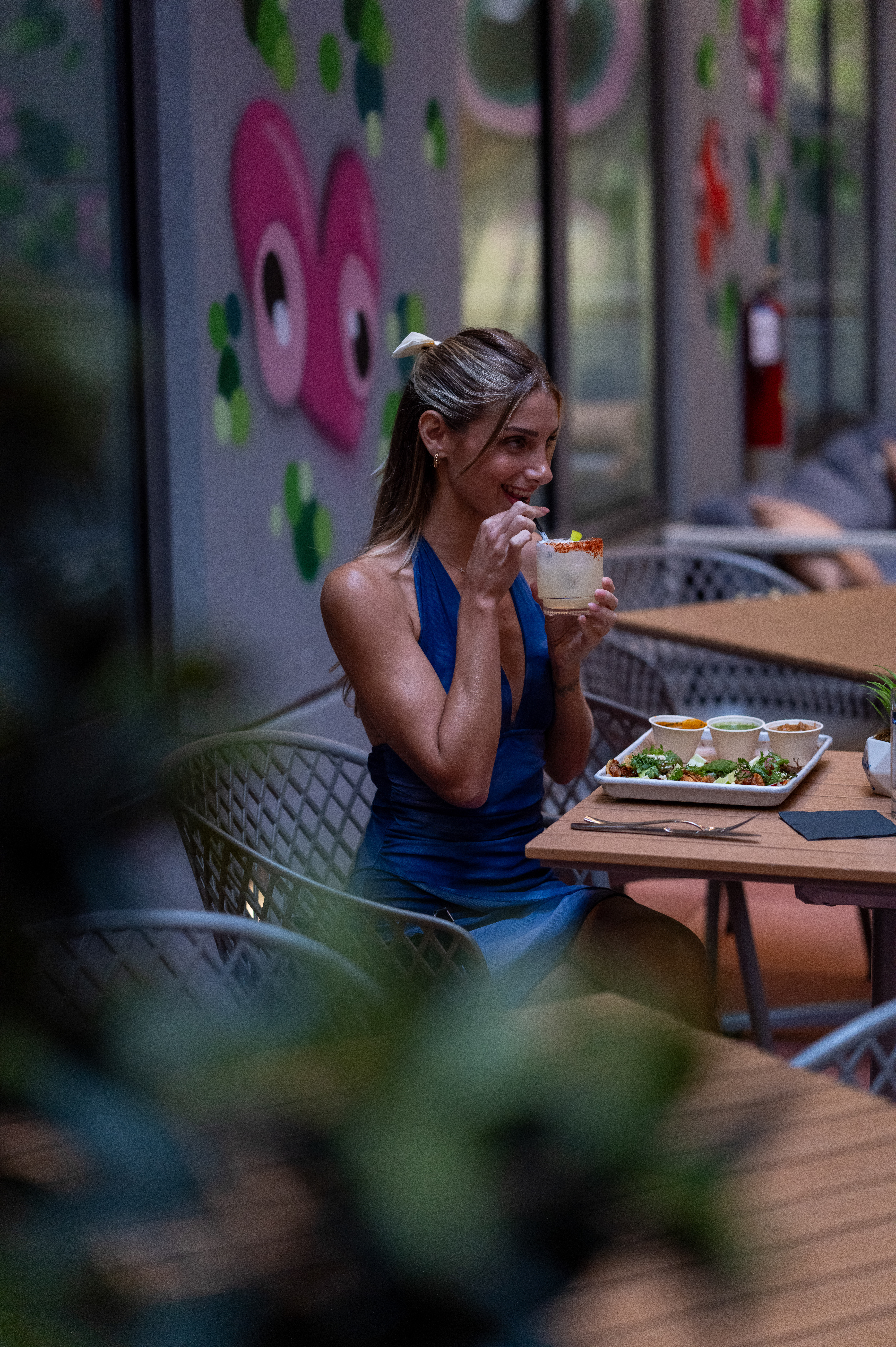 Woman enjoying margarita & appetizers at a vibrant outdoor bar.