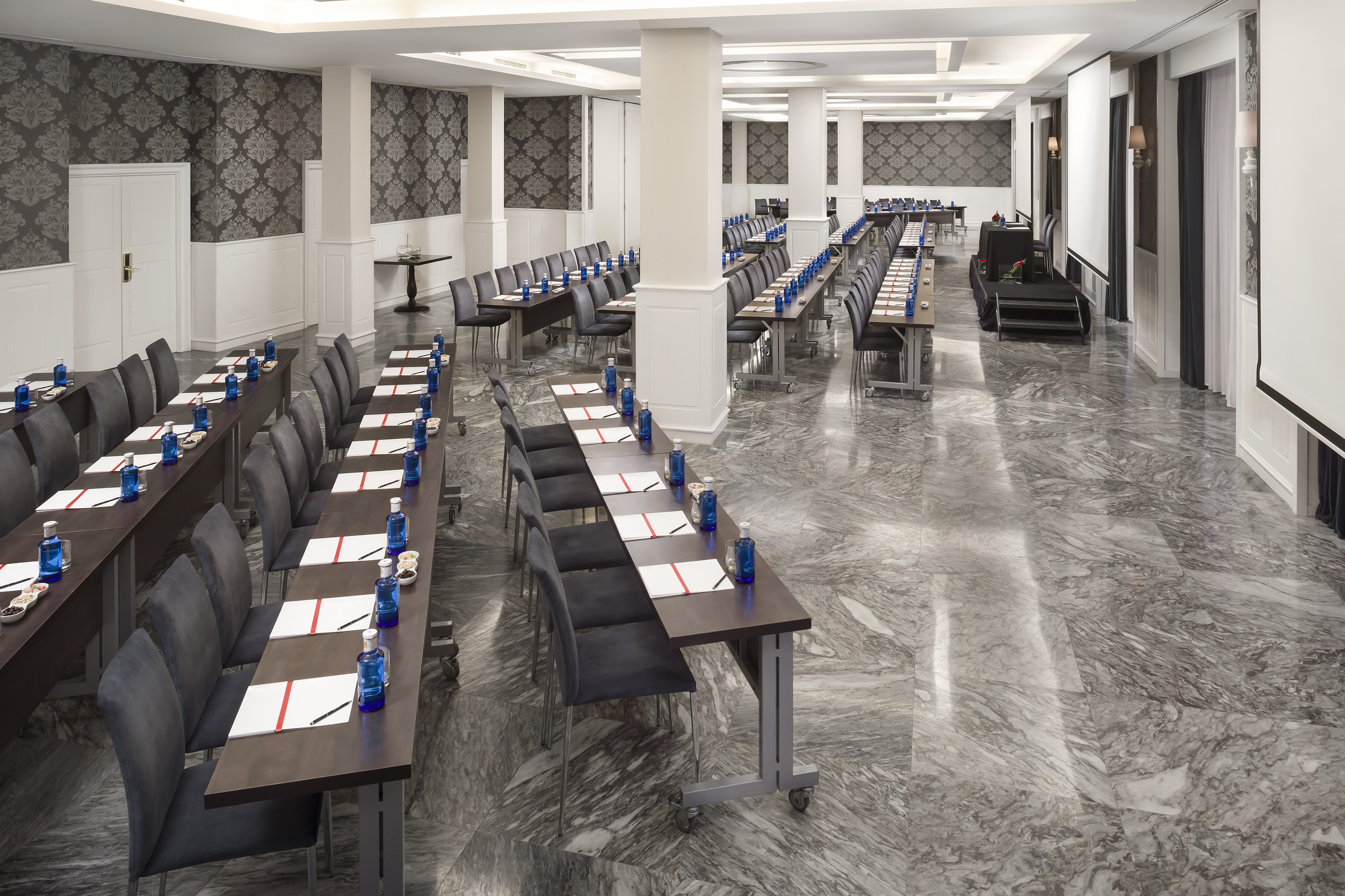 Spacious conference room setup with tables, chairs, screens, and marble floor.