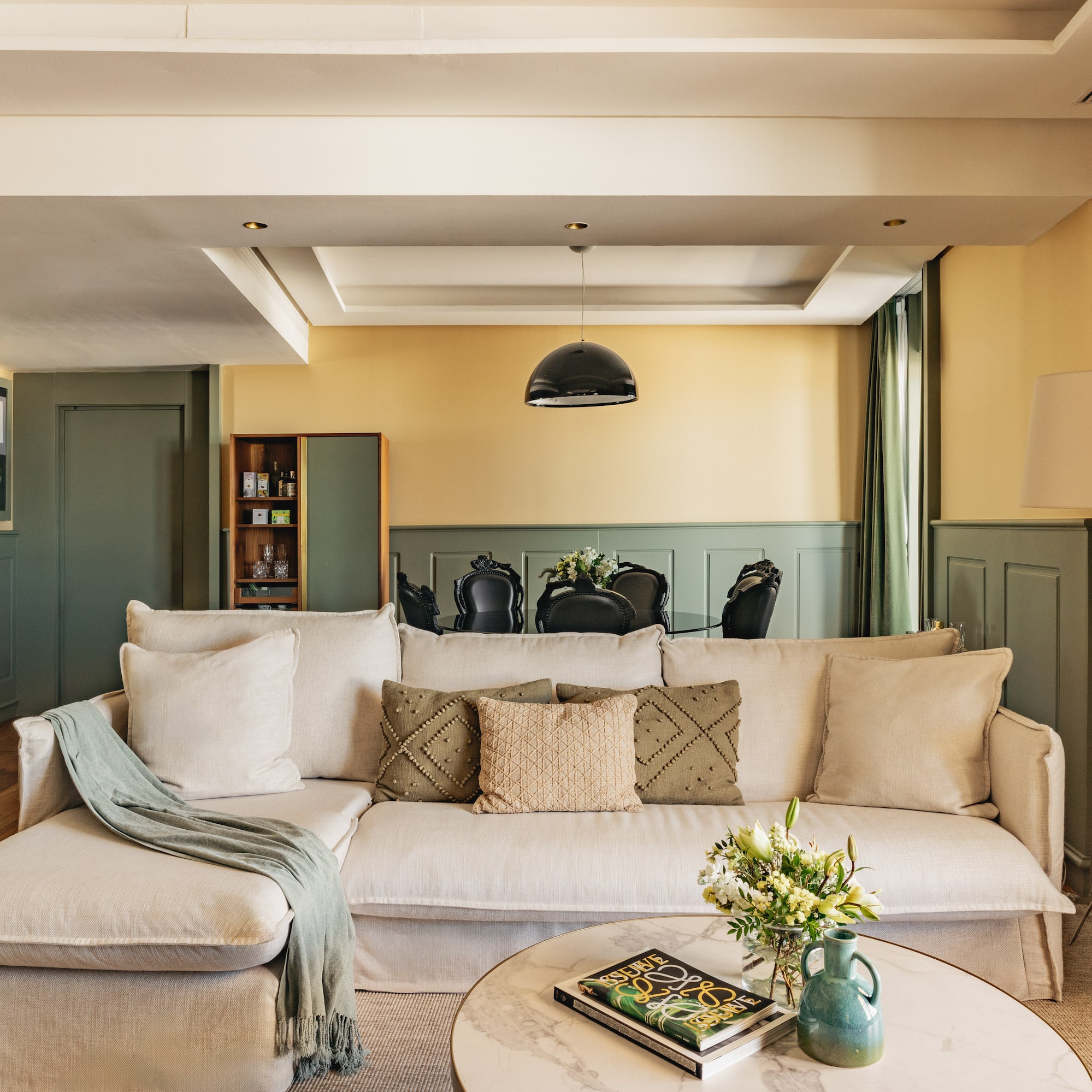 Salón moderno con sofá beige, paredes bicolor y comedor elegante.