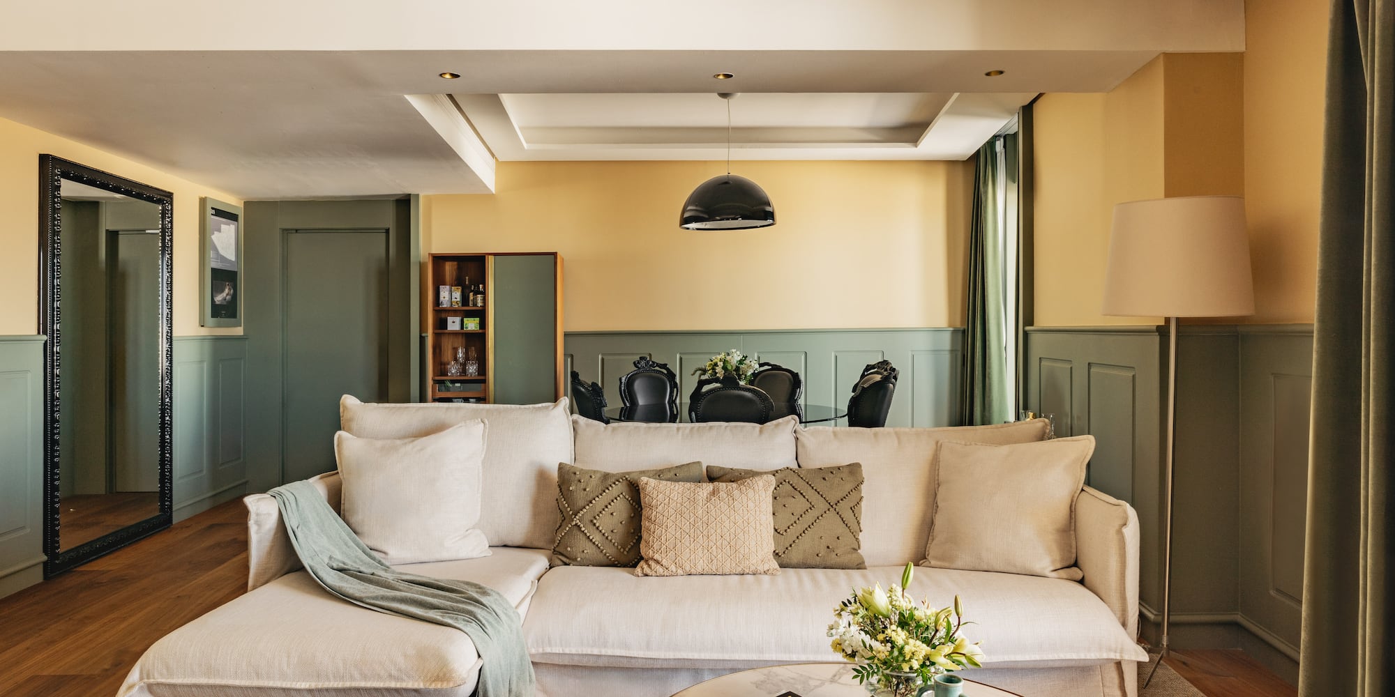 Salón moderno con sofá beige, paredes bicolor y comedor elegante.