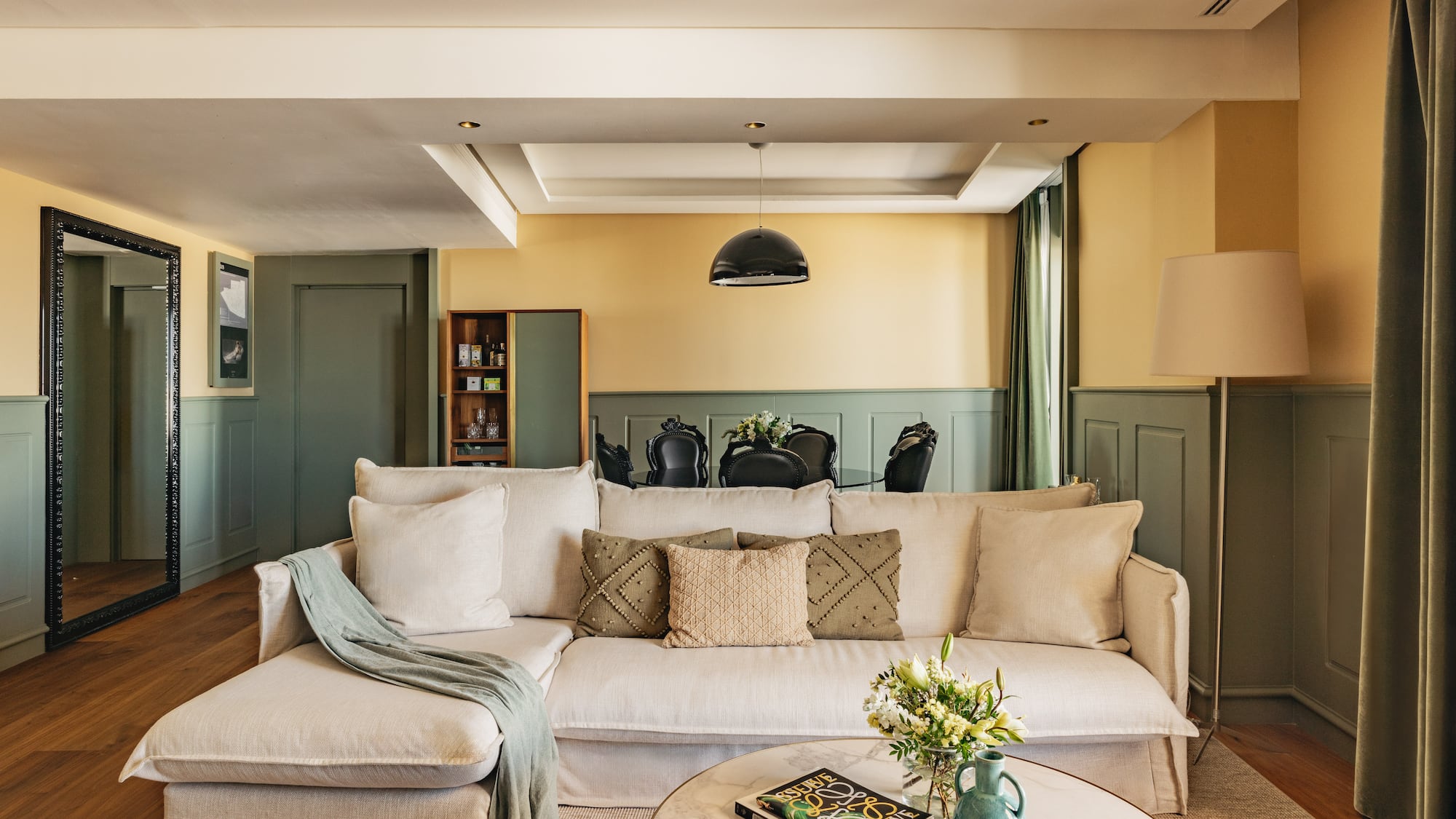 Salón moderno con sofá beige, paredes bicolor y comedor elegante.