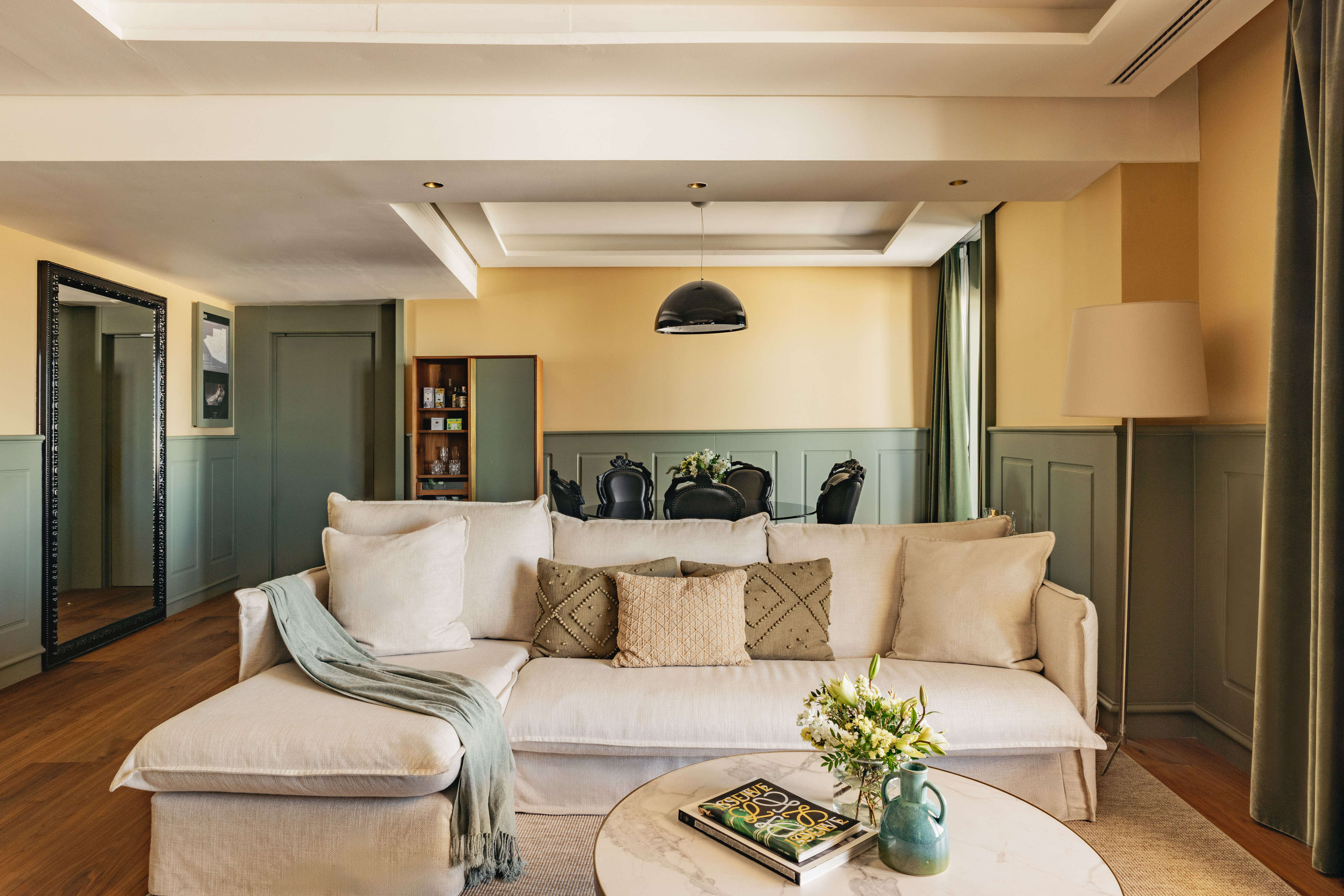 Salón moderno con sofá beige, paredes bicolor y comedor elegante.