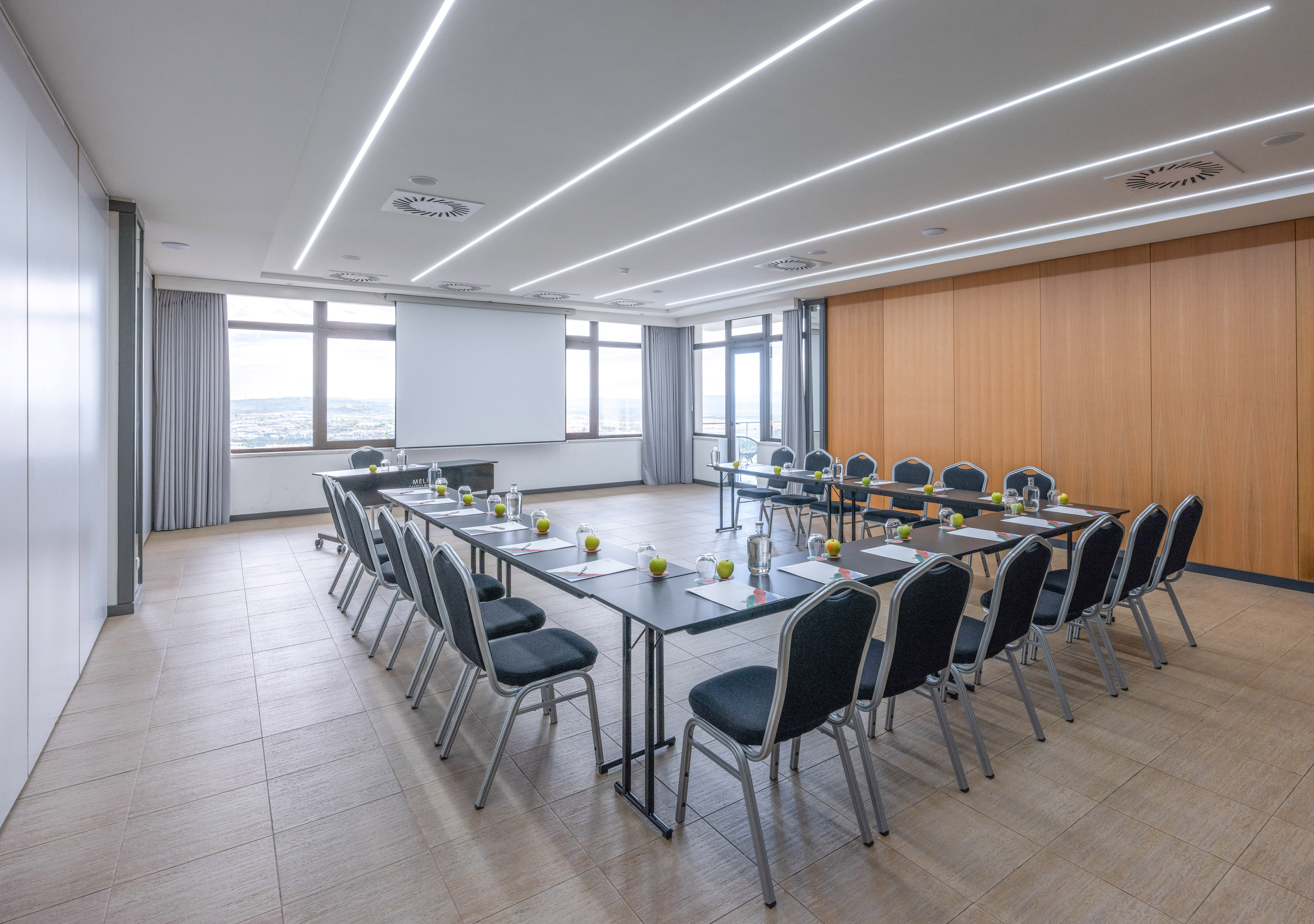 Modern conference room with U-shaped table, projector screen, and city view.