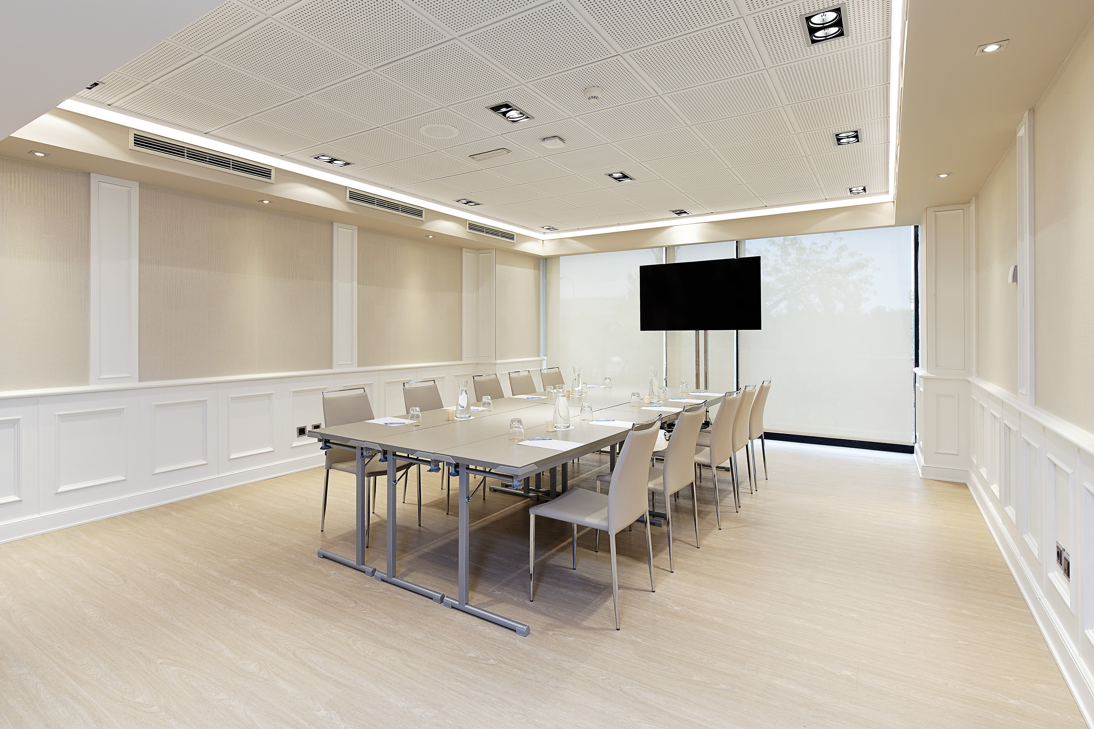 Modern meeting room with table, chairs, TV, and light wood floor.