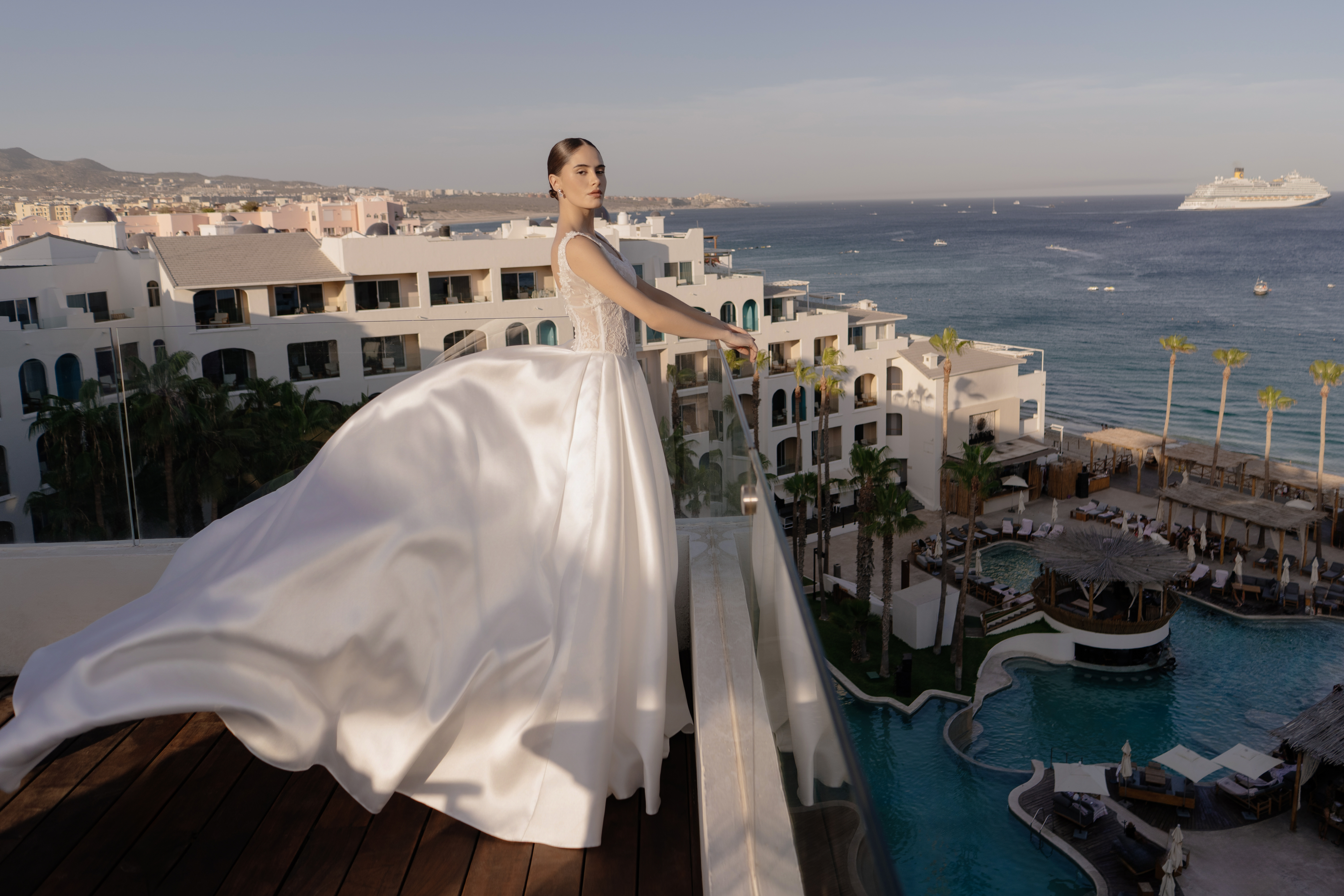Elegant bride in flowing white gown on luxury resort balcony, ocean view.
