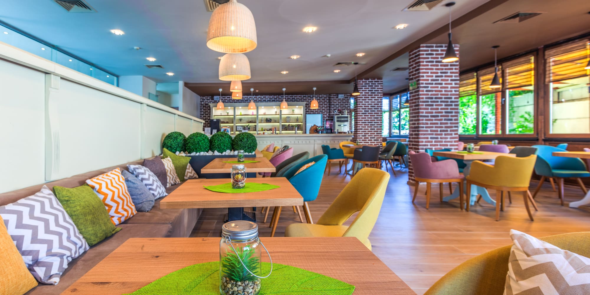 Modern cafe with colorful seating, wooden tables, and exposed brick walls.