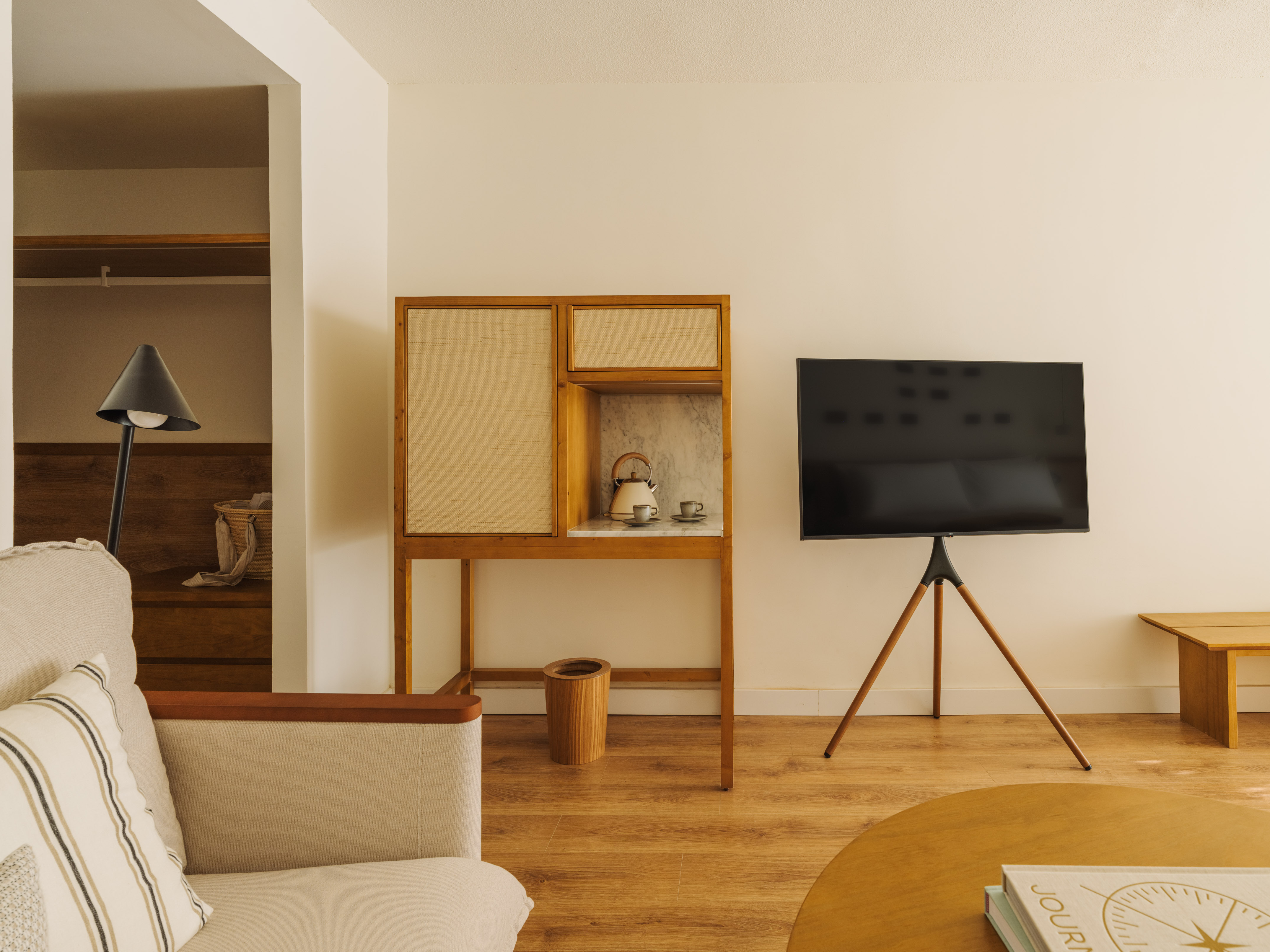 Contemporary living space with beige sofa, rattan console, and tripod TV.