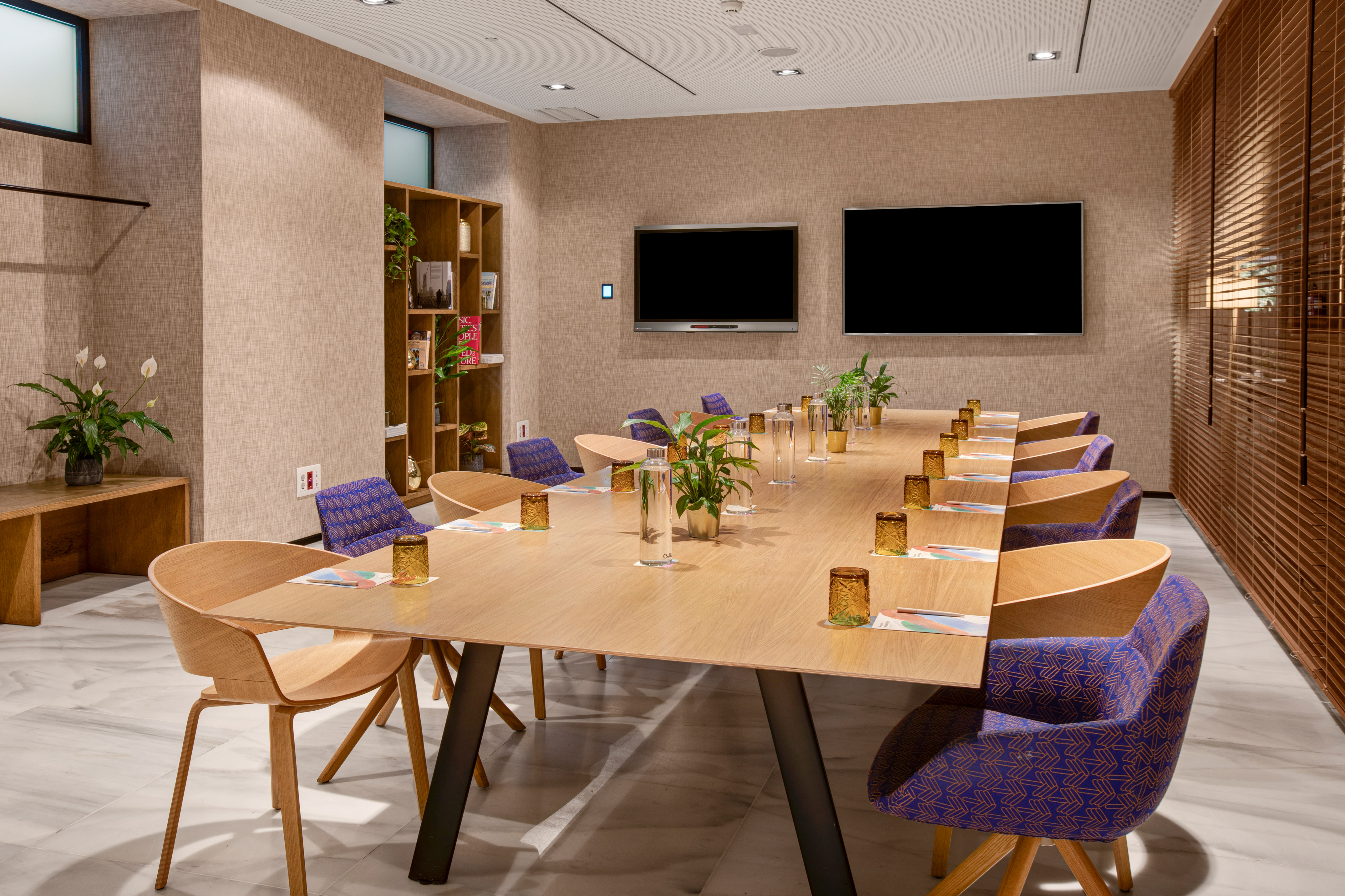 Modern conference room with long table, purple chairs, and dual screens.
