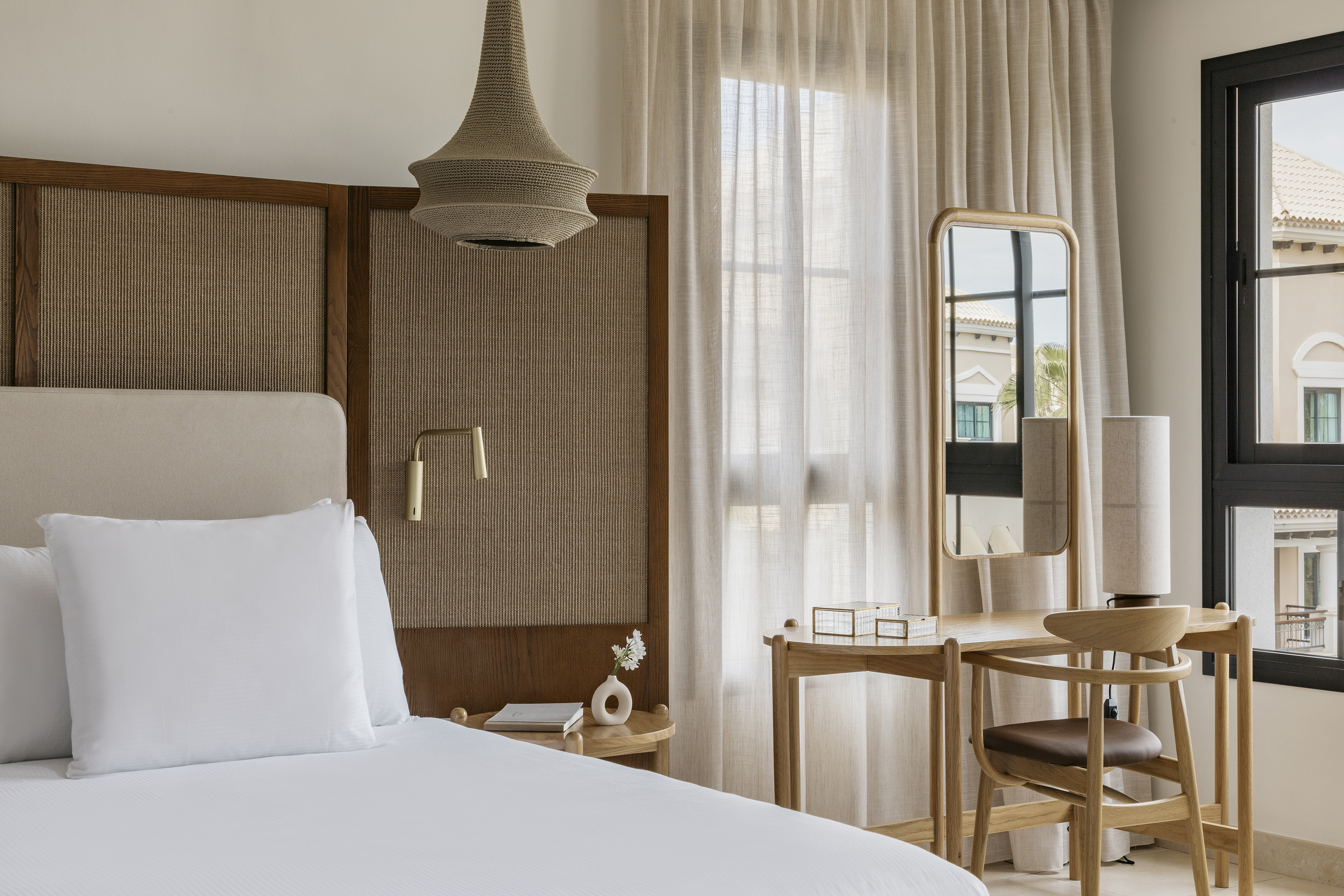 Modern neutral bedroom with rattan headboard, woven pendant, wooden vanity.