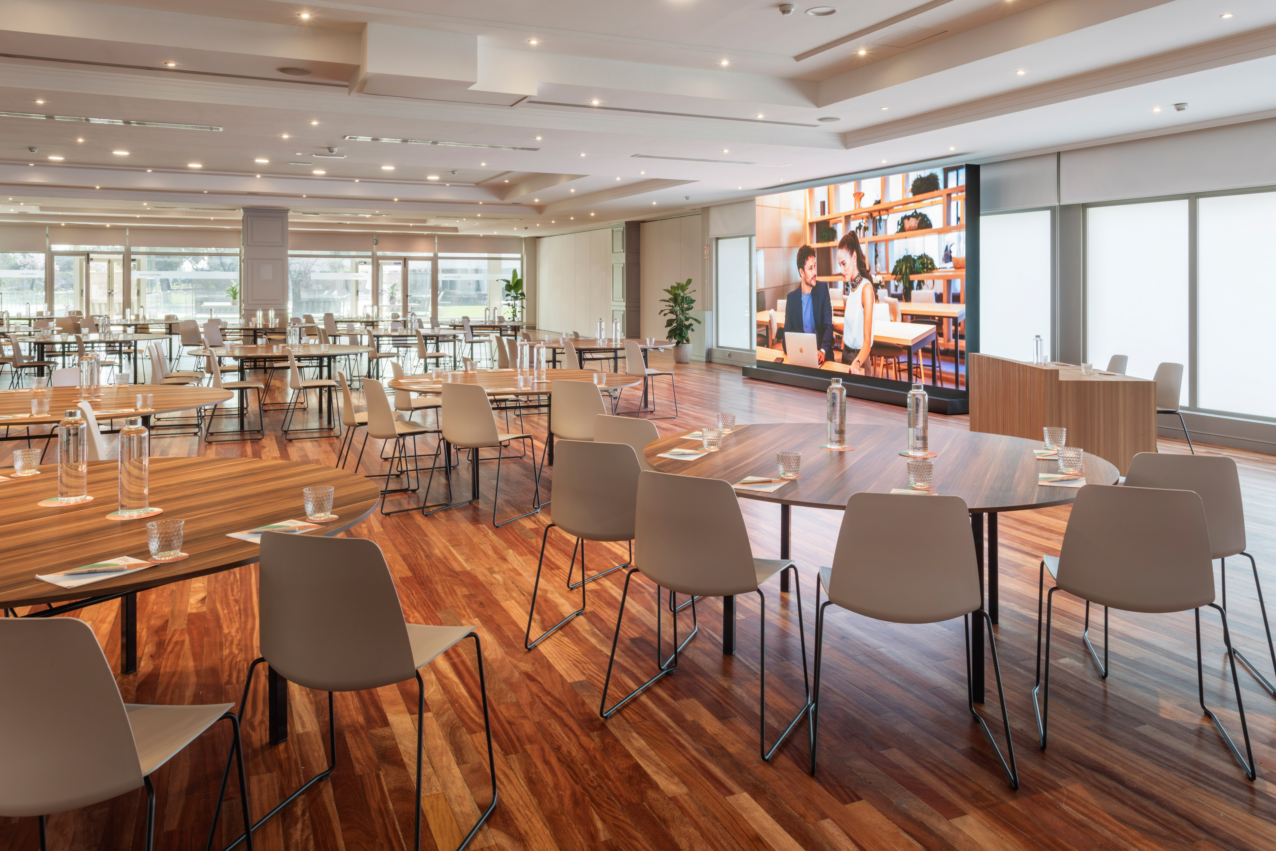 Modern conference room with wooden tables, chairs, and large LED screen display.