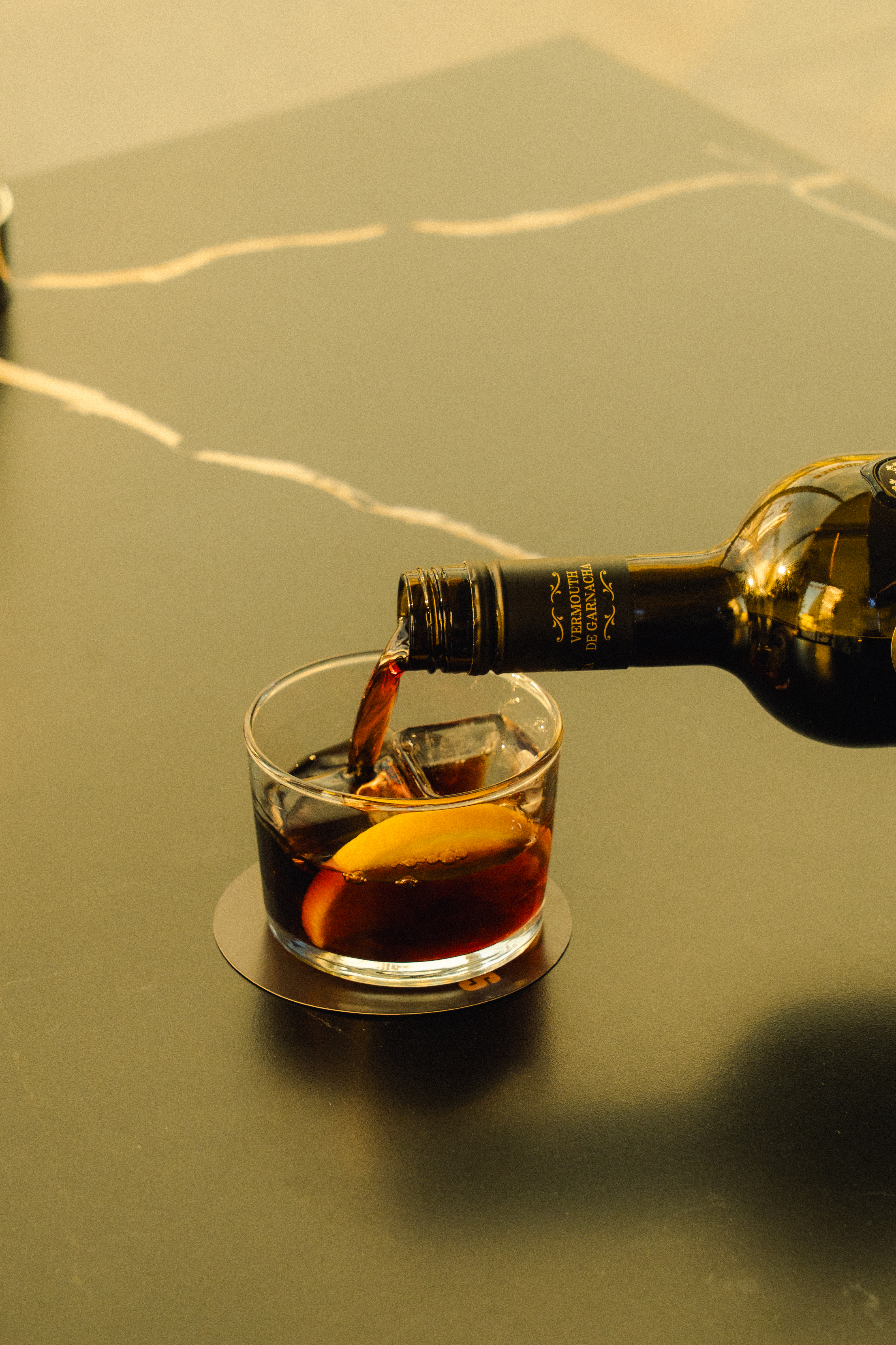 Pouring red vermouth from a Garnacha bottle into a glass with ice and orange.