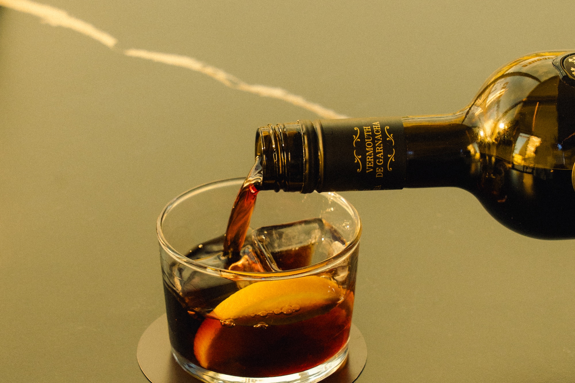 Pouring red vermouth from a Garnacha bottle into a glass with ice and orange.