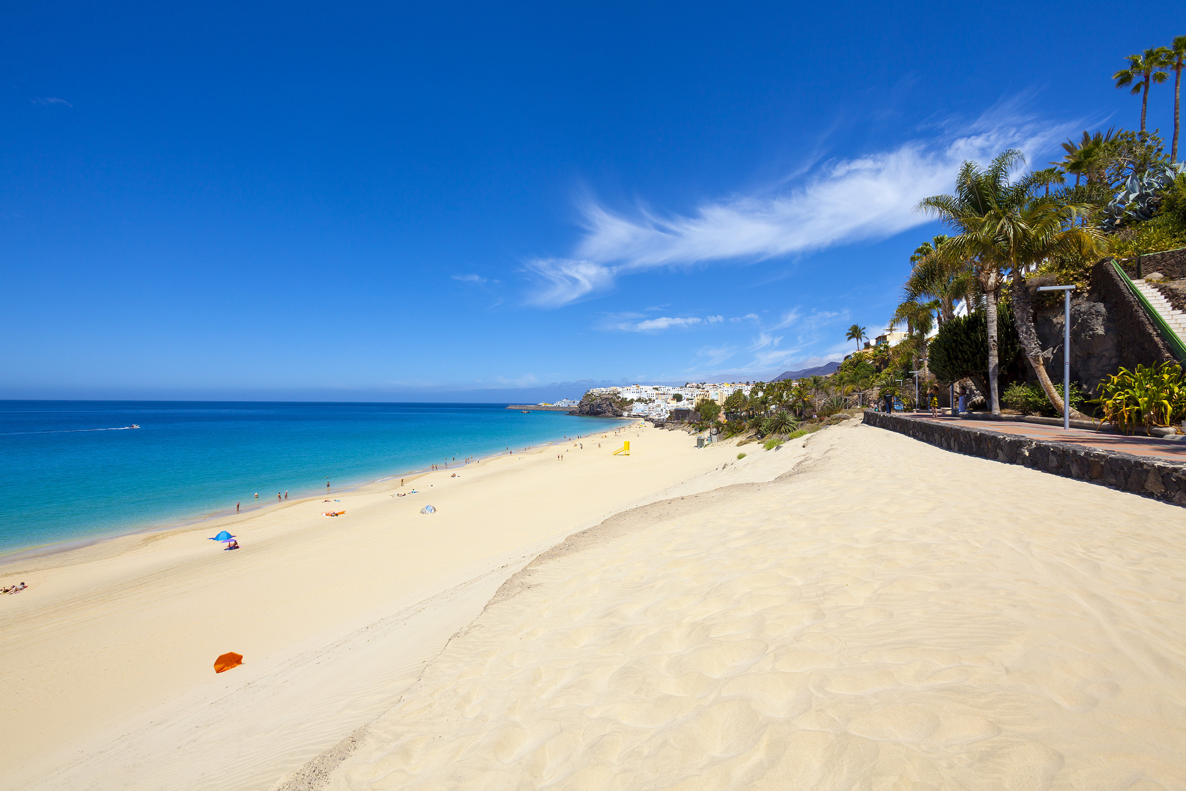 Sunny white sand beach with turquoise ocean, distant town, and palm trees.