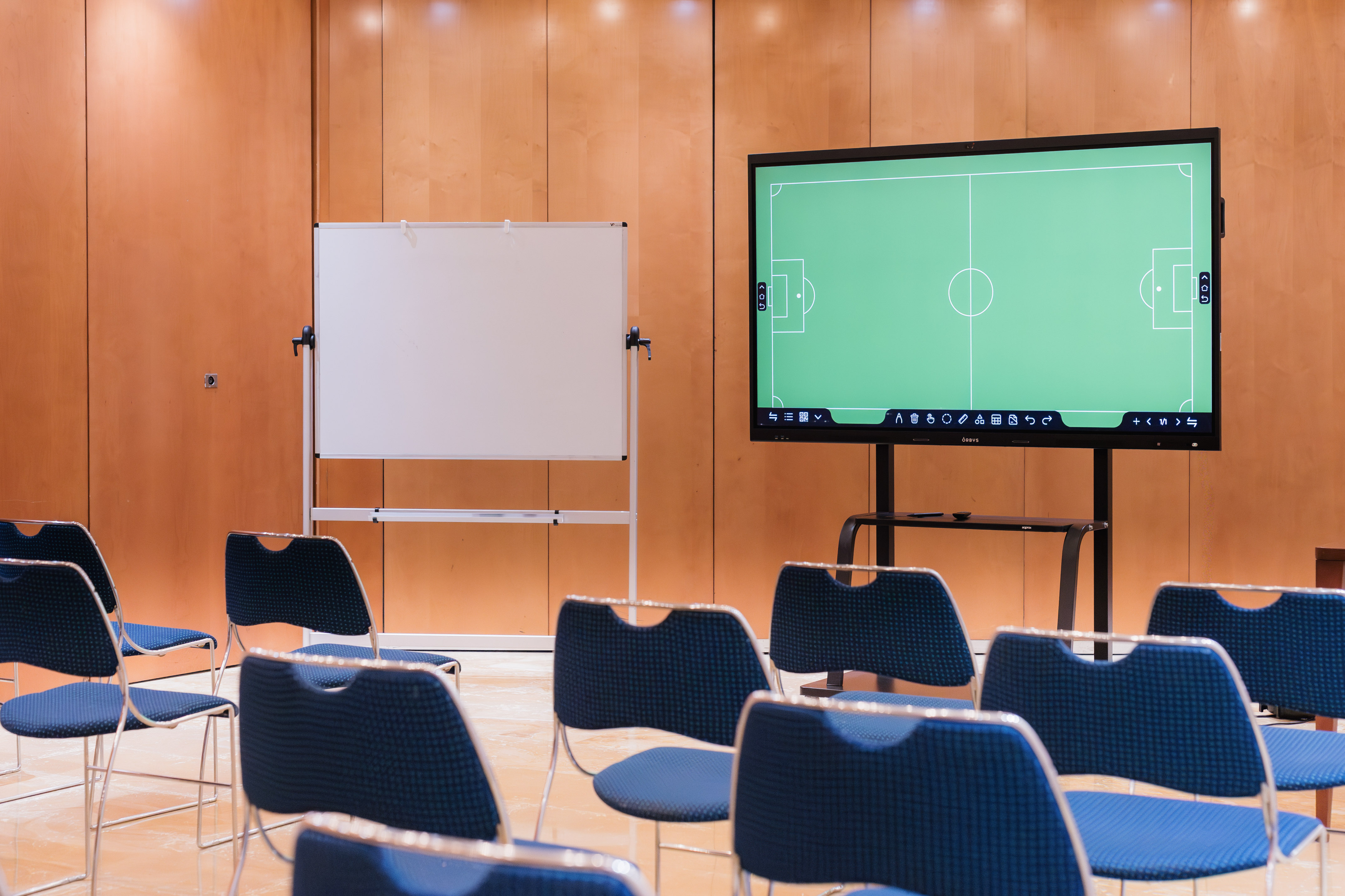 Interactive display with soccer field, whiteboard, and blue chairs in a meeting room.