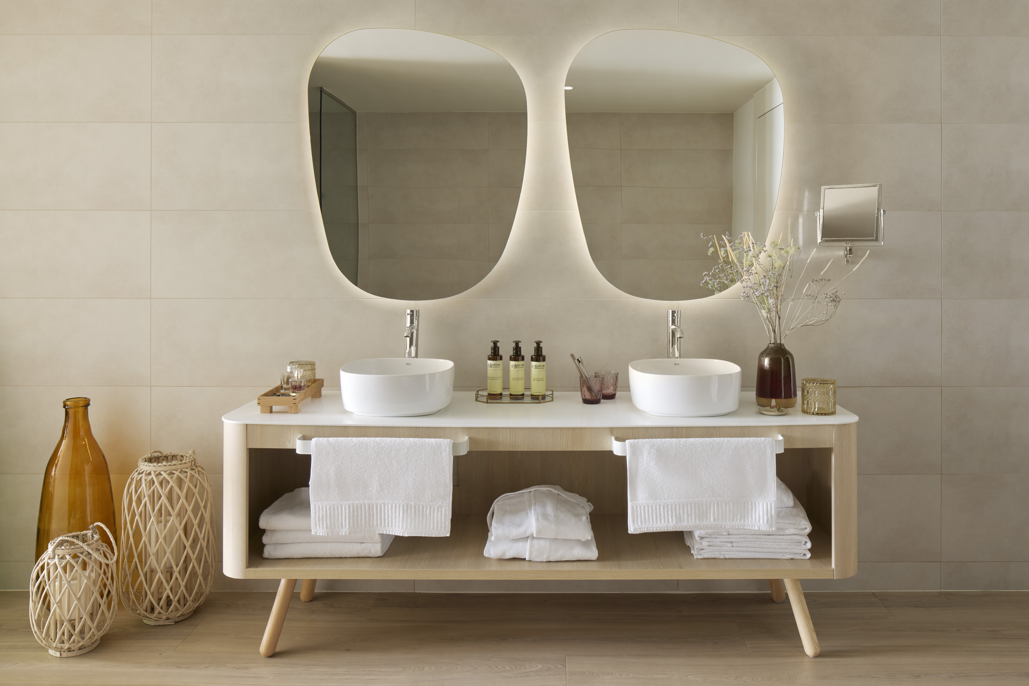 Hotel bathroom with twin sinks, illuminated organic mirrors, and wood vanity.