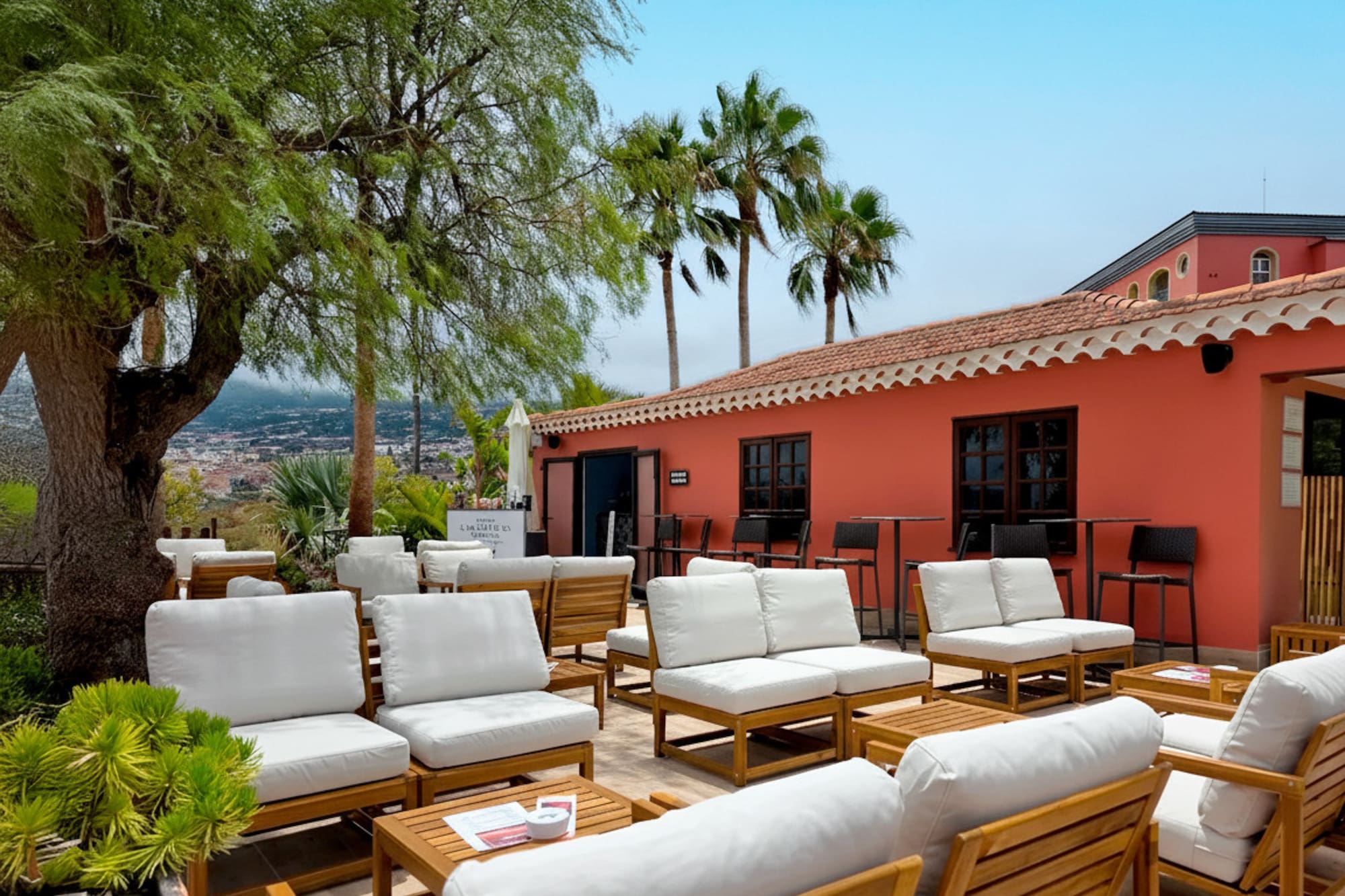 Tropical outdoor lounge patio with white seating, coral building, and palm trees.