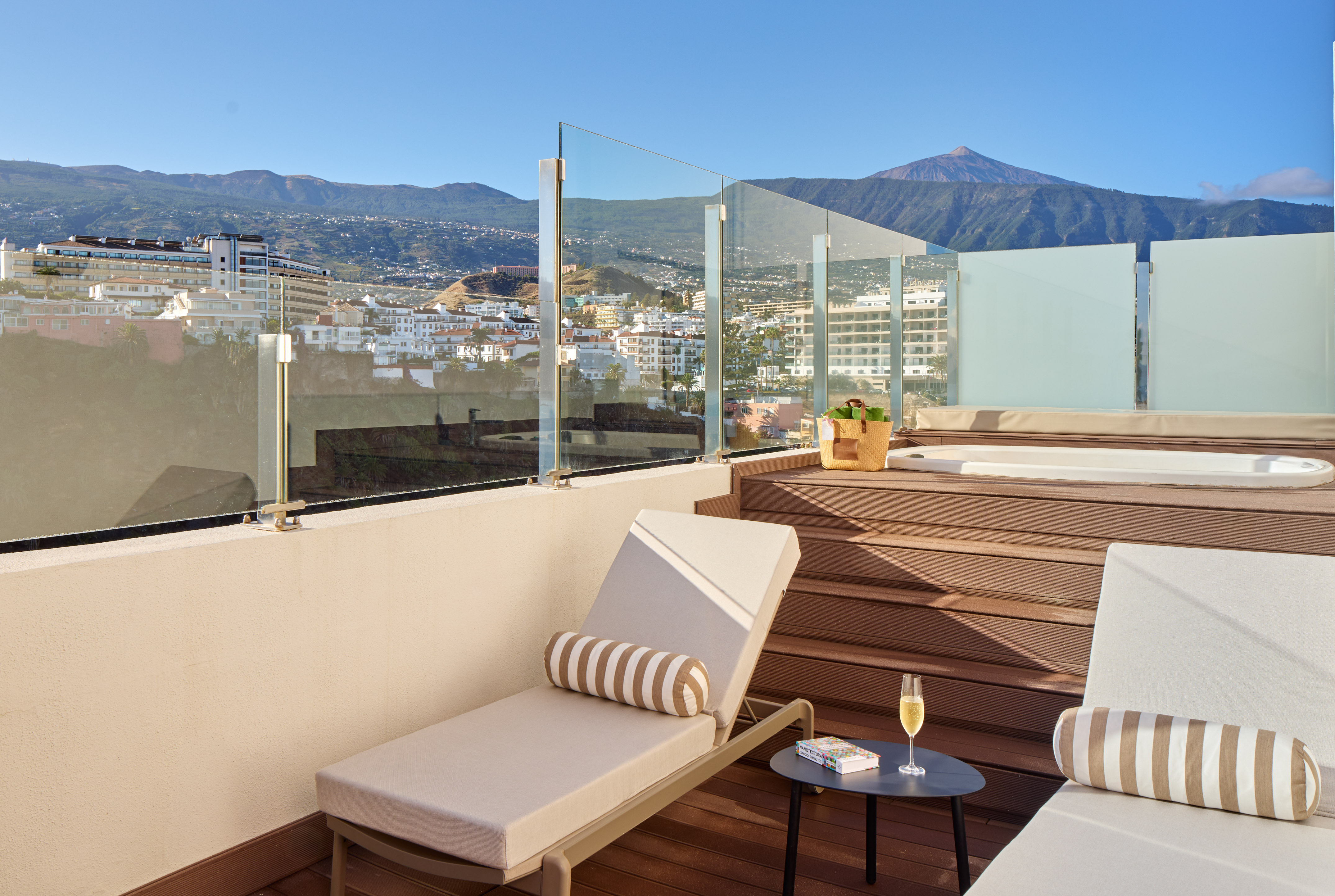 Rooftop terrace with hot tub, sun loungers, city, and mountain view.