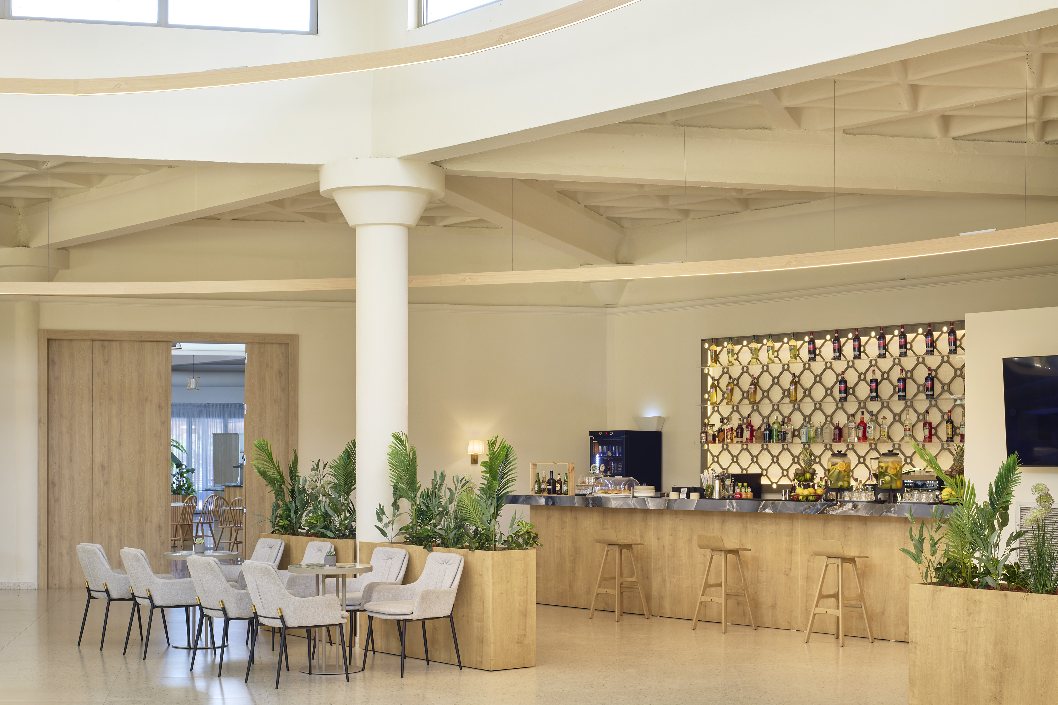 Modern hotel bar with lounge seating, bar stools, drinks, and plants.