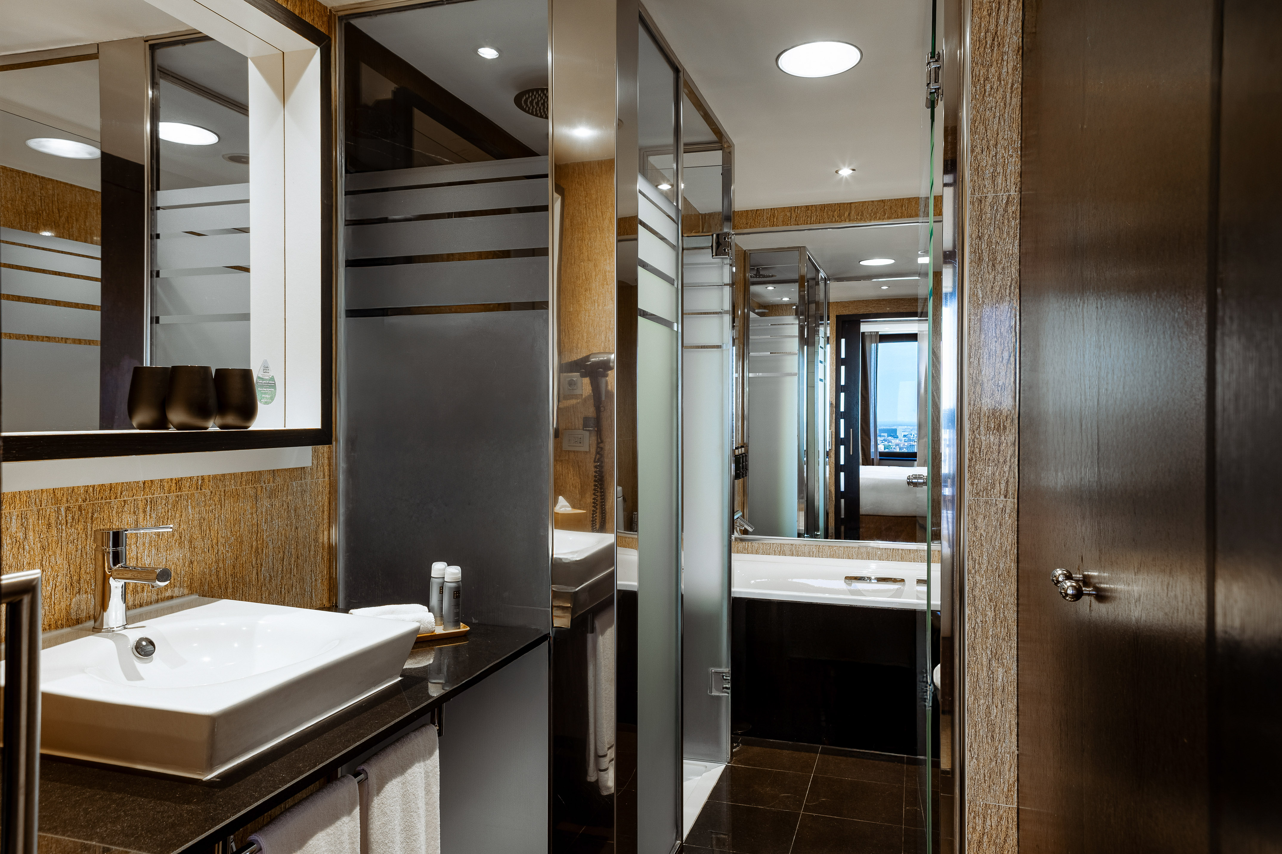 Elegant hotel bathroom with sink, glass shower, bathtub, and modern design.