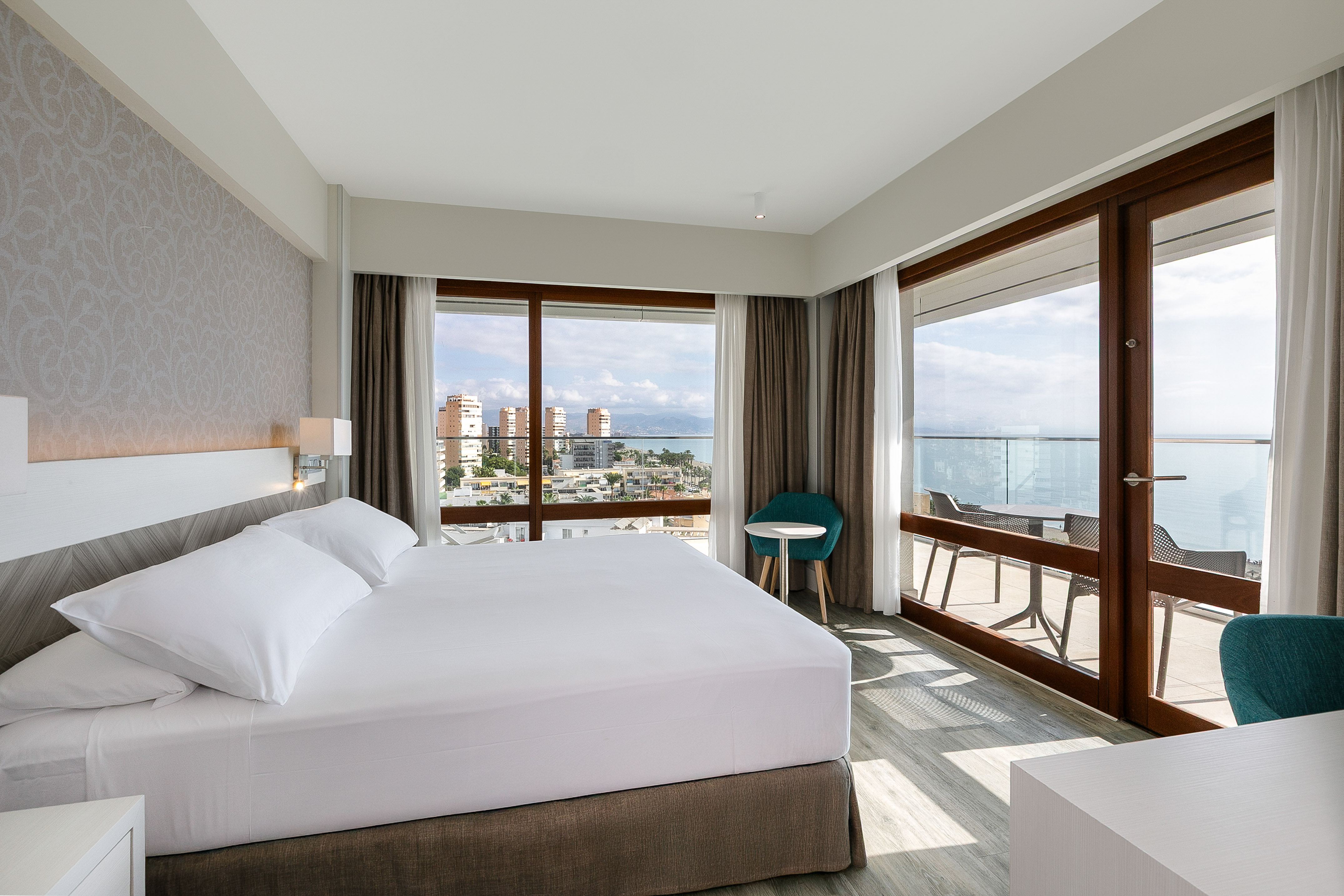 Modern hotel room with king bed, balcony, and panoramic sea & city views.