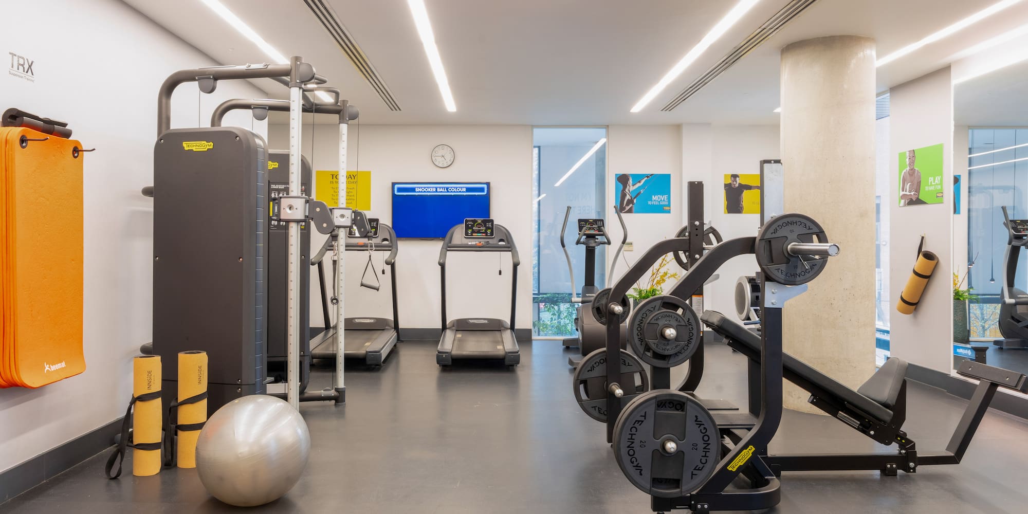 Modern gym interior with Technogym treadmills, weights, TRX, and yoga mats.