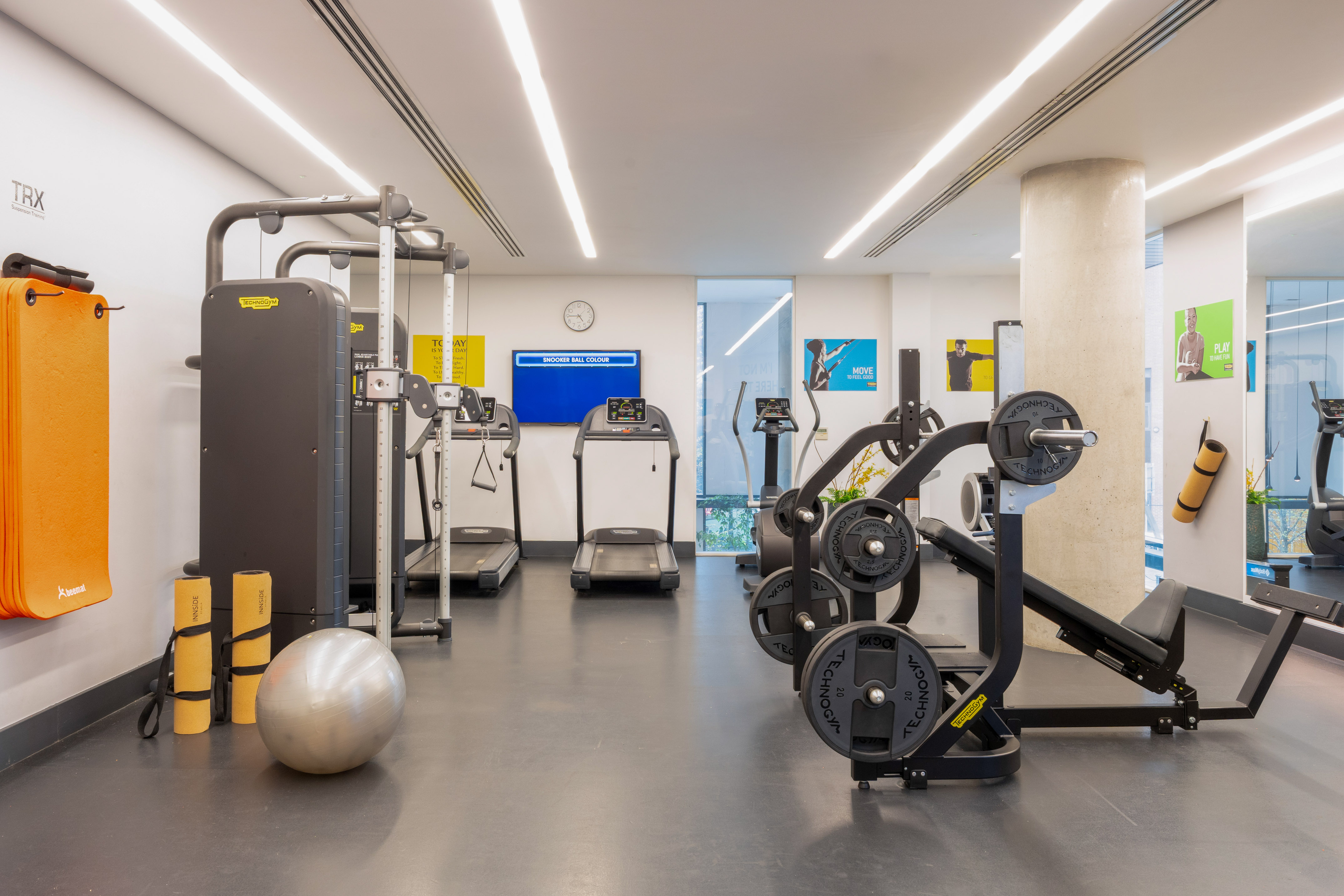 Modern gym interior with Technogym treadmills, weights, TRX, and yoga mats.