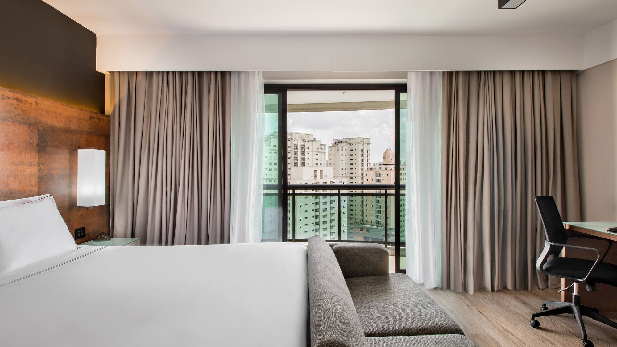 a room with a bed and couches and a window with a view of a city