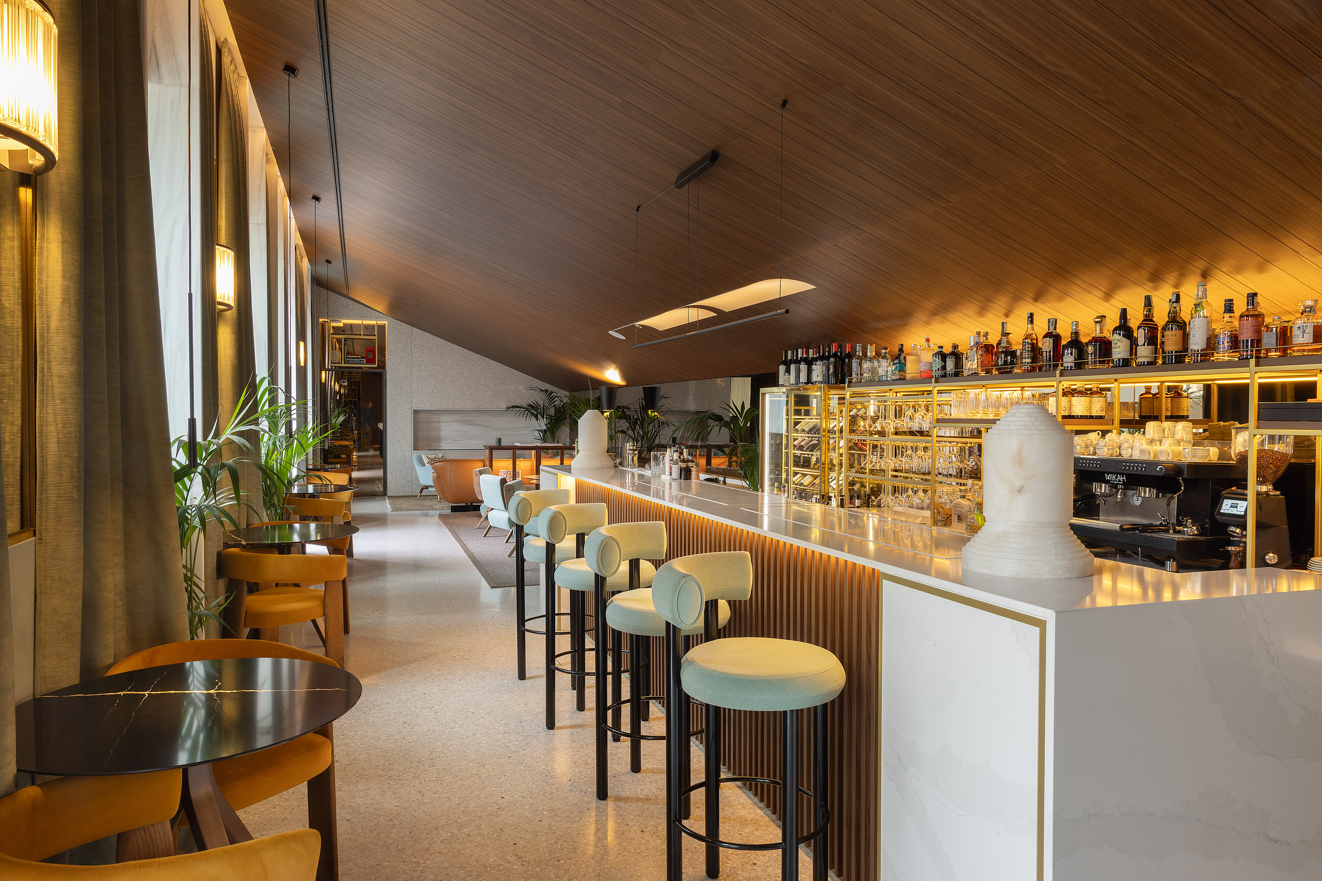 Upscale hotel bar featuring marble counter, green stools, and elegant wooden ceiling.