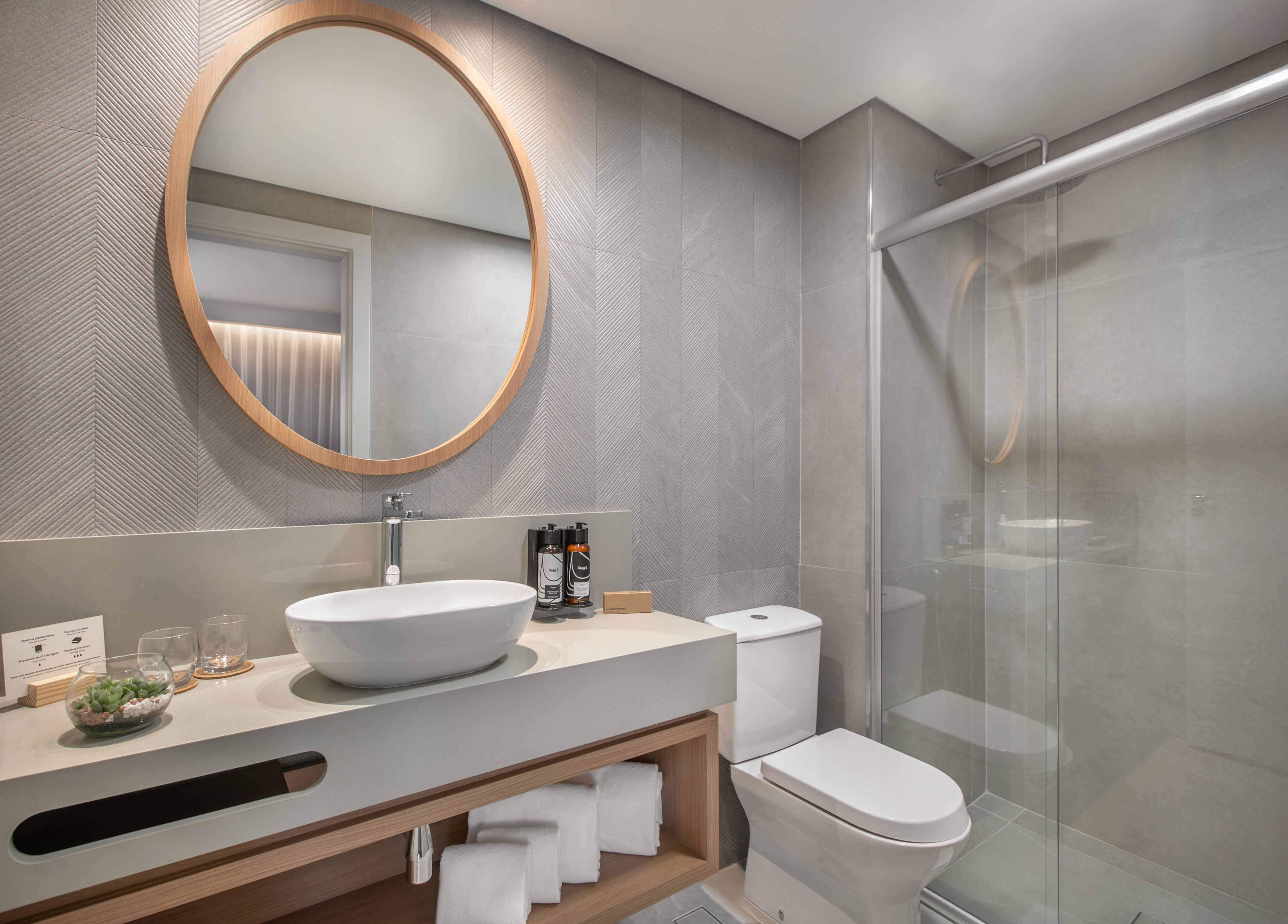 Modern gray bathroom with vessel sink, round mirror, toilet, and glass shower.