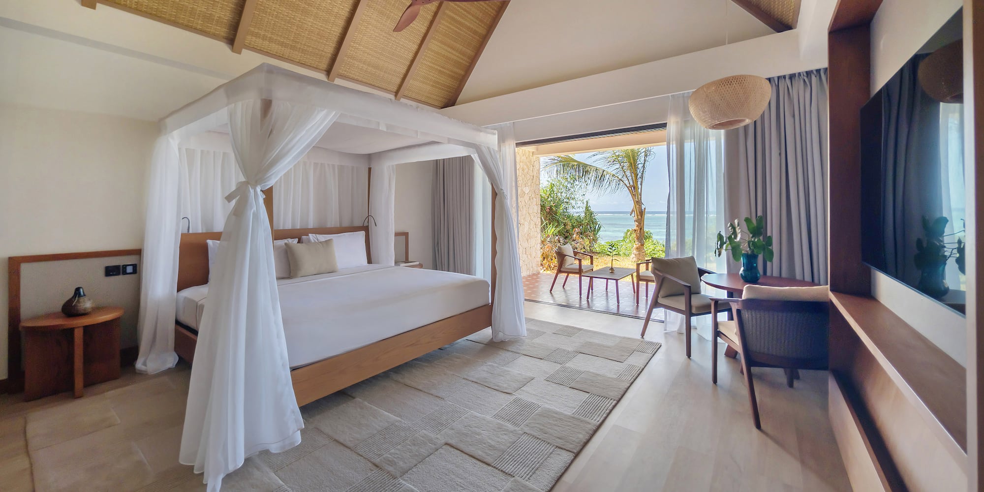Luxury resort bedroom with canopy bed, ocean view, and thatched ceiling.