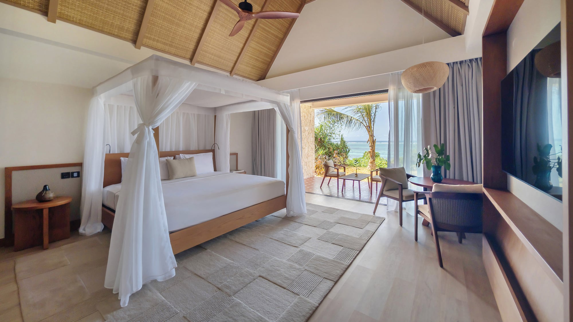 Luxury resort bedroom with canopy bed, ocean view, and thatched ceiling.