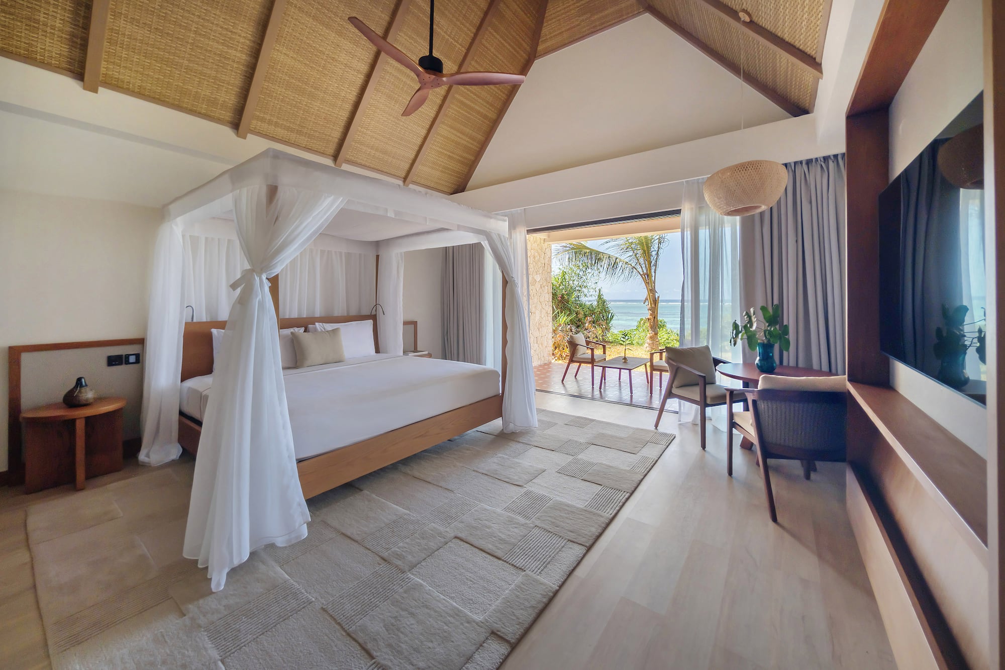Luxury resort bedroom with canopy bed, ocean view, and thatched ceiling.