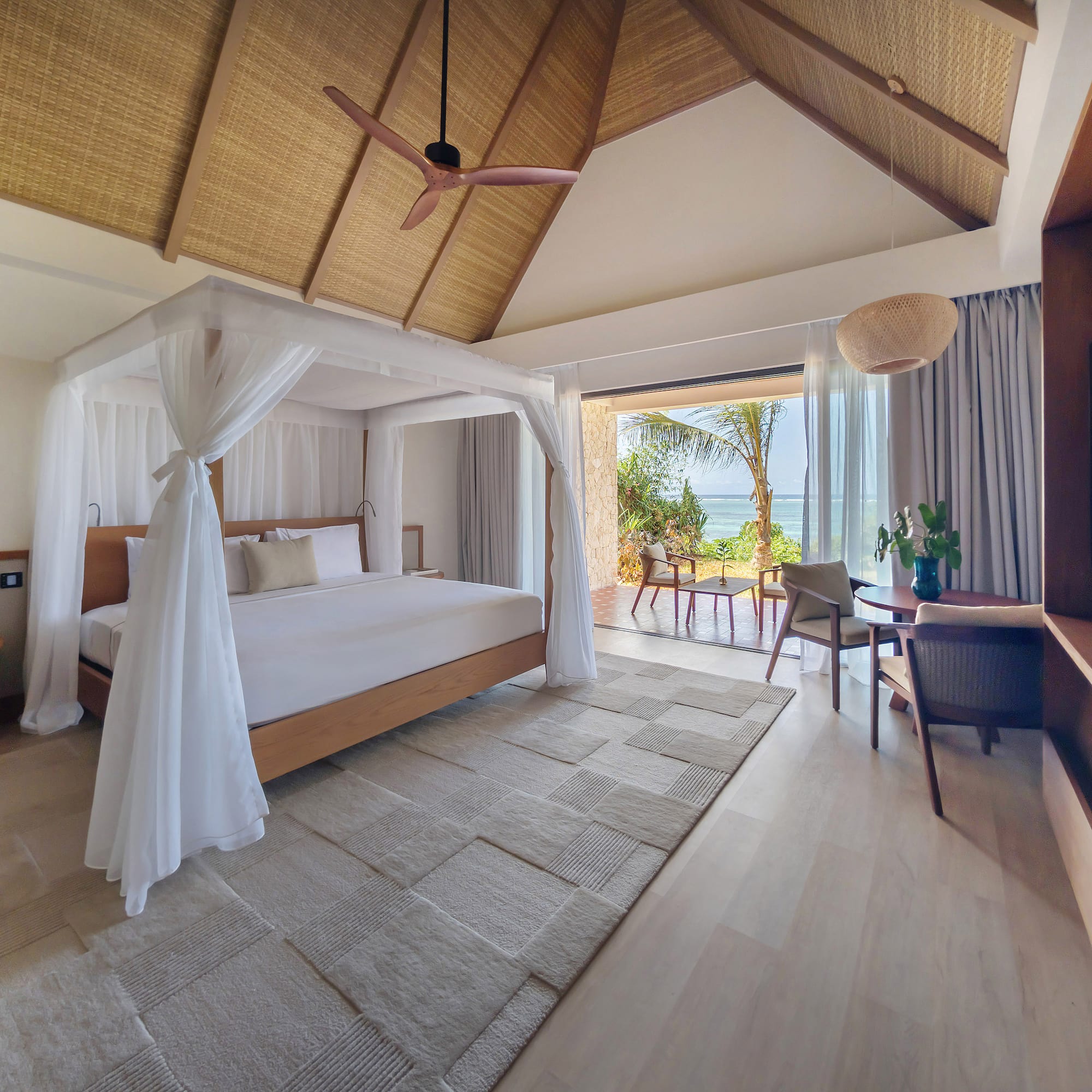 Luxury resort bedroom with canopy bed, ocean view, and thatched ceiling.