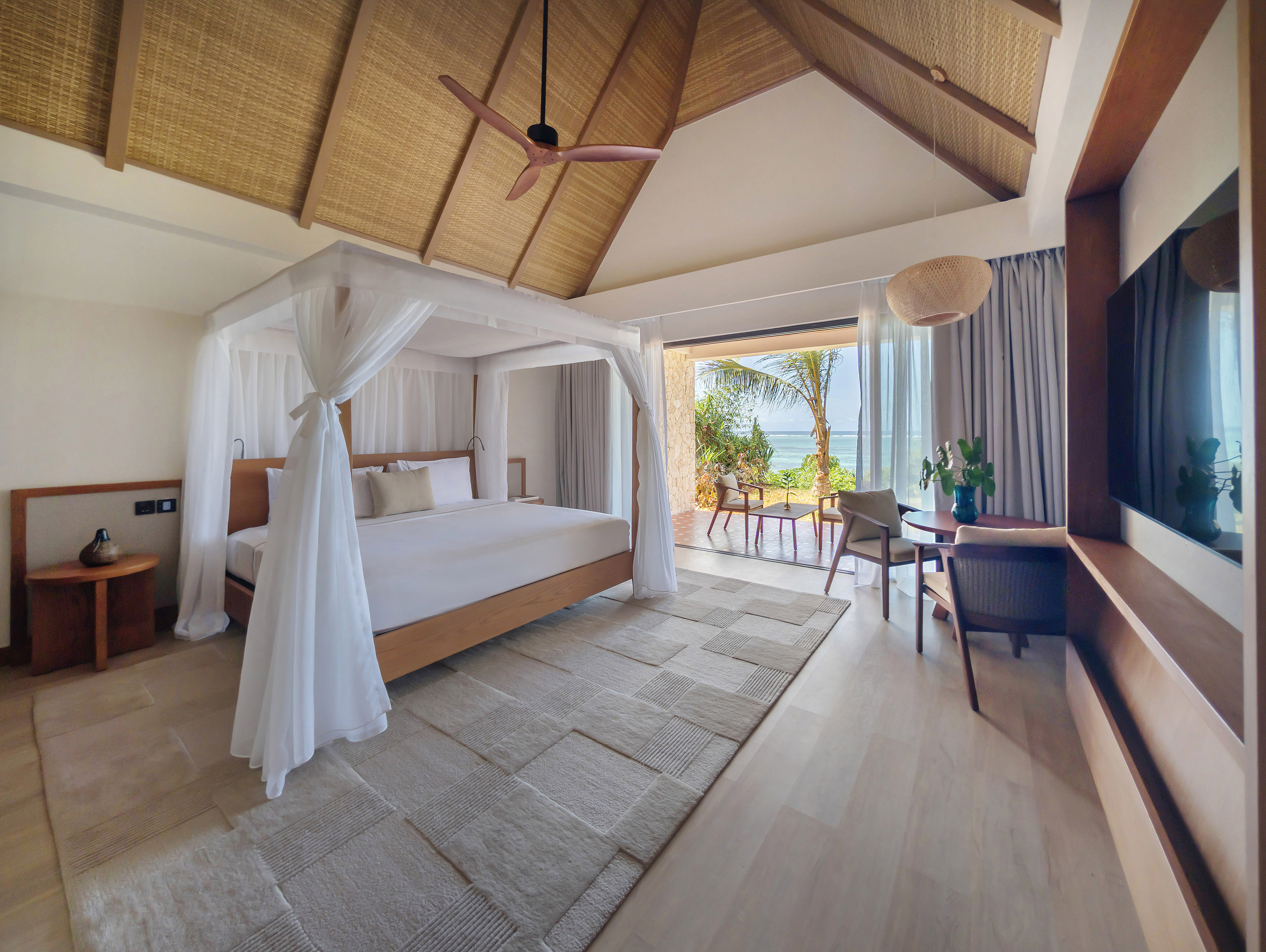 Luxury resort bedroom with canopy bed, ocean view, and thatched ceiling.