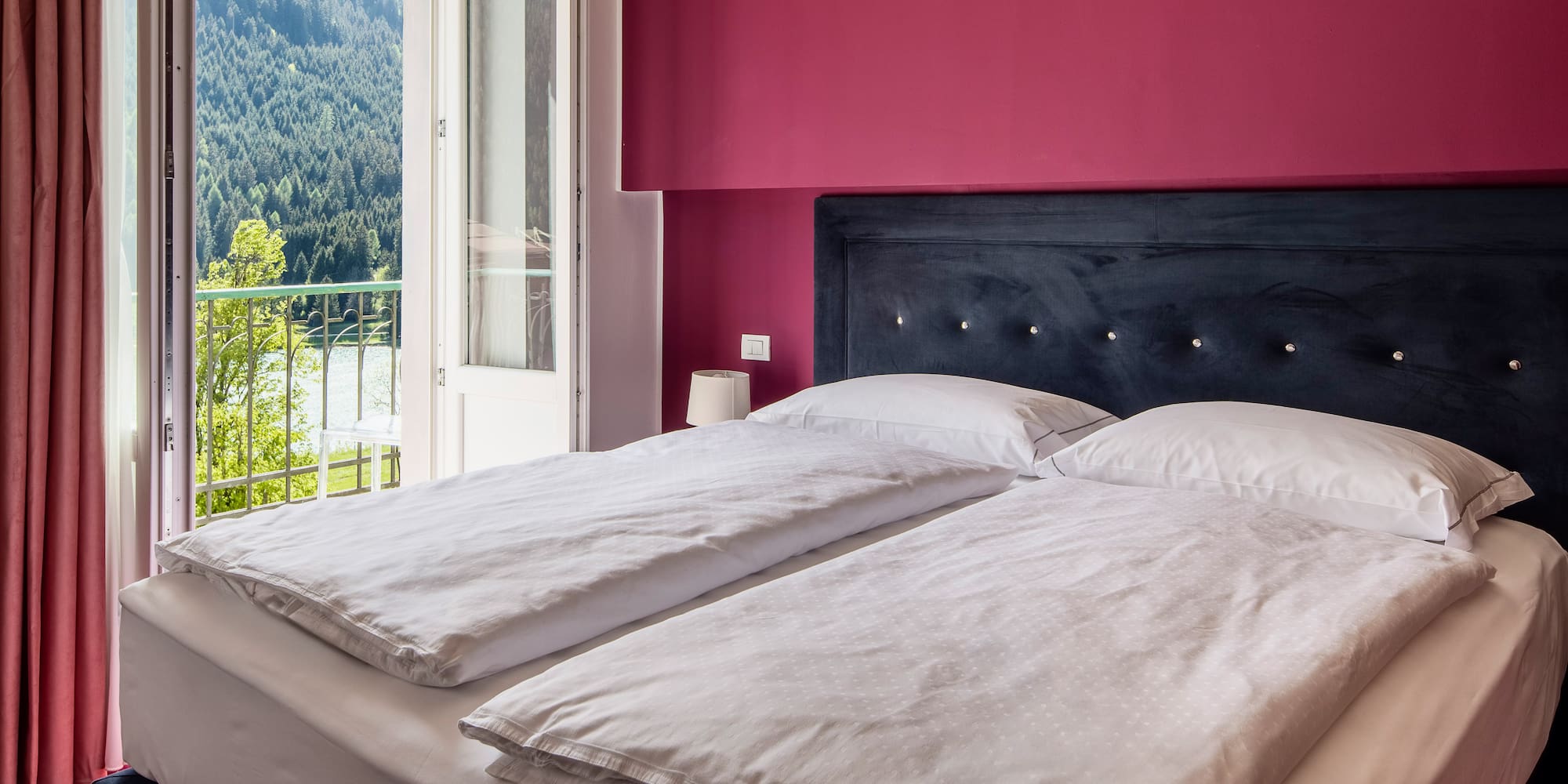 Bedroom with magenta wall, bed, balcony lake and forest view.