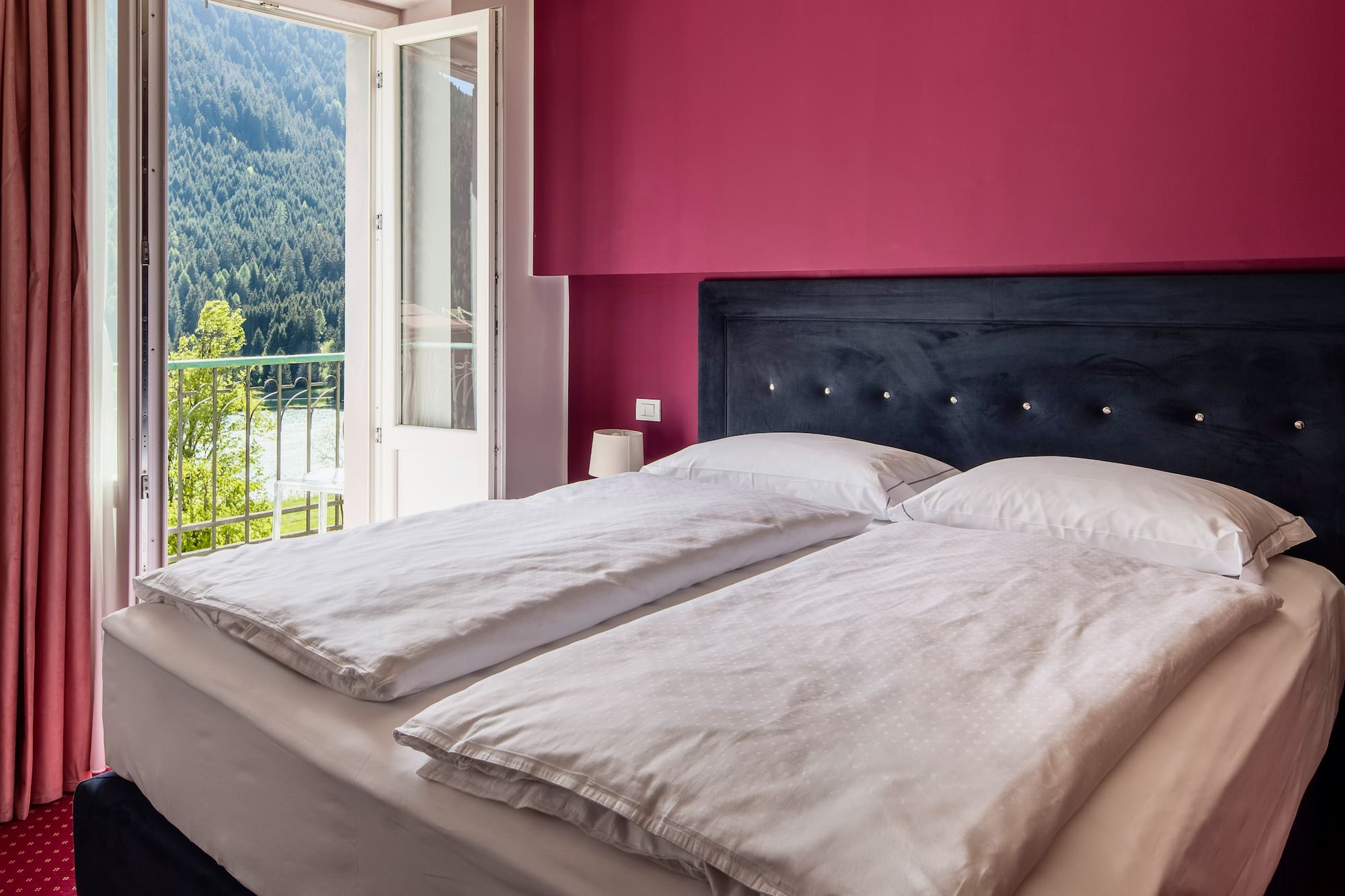 Bedroom with magenta wall, bed, balcony lake and forest view.