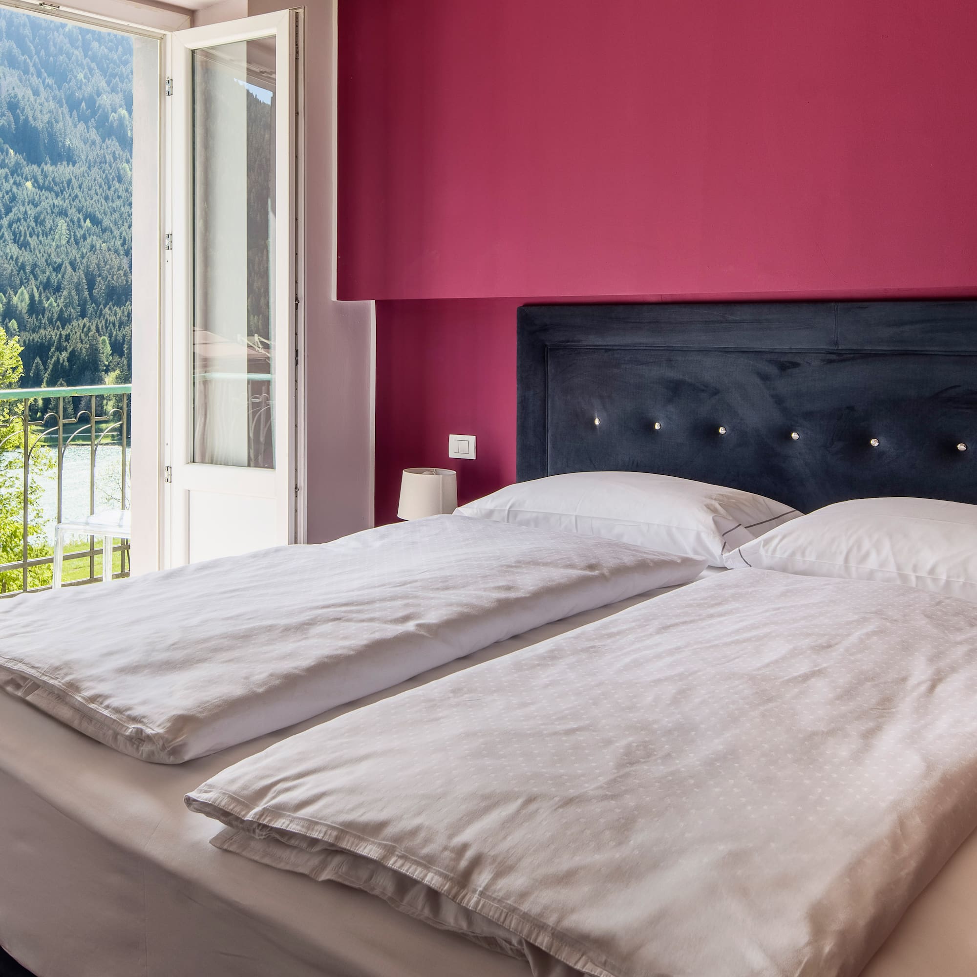 Bedroom with magenta wall, bed, balcony lake and forest view.