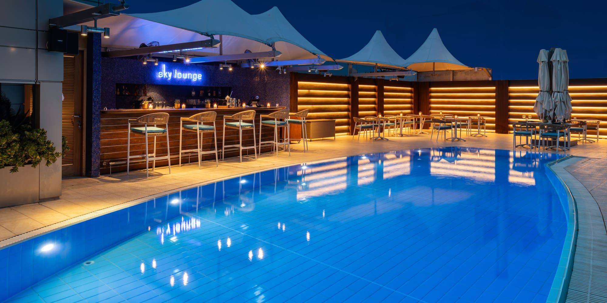 Sky Lounge rooftop bar with illuminated pool and poolside dining at night.