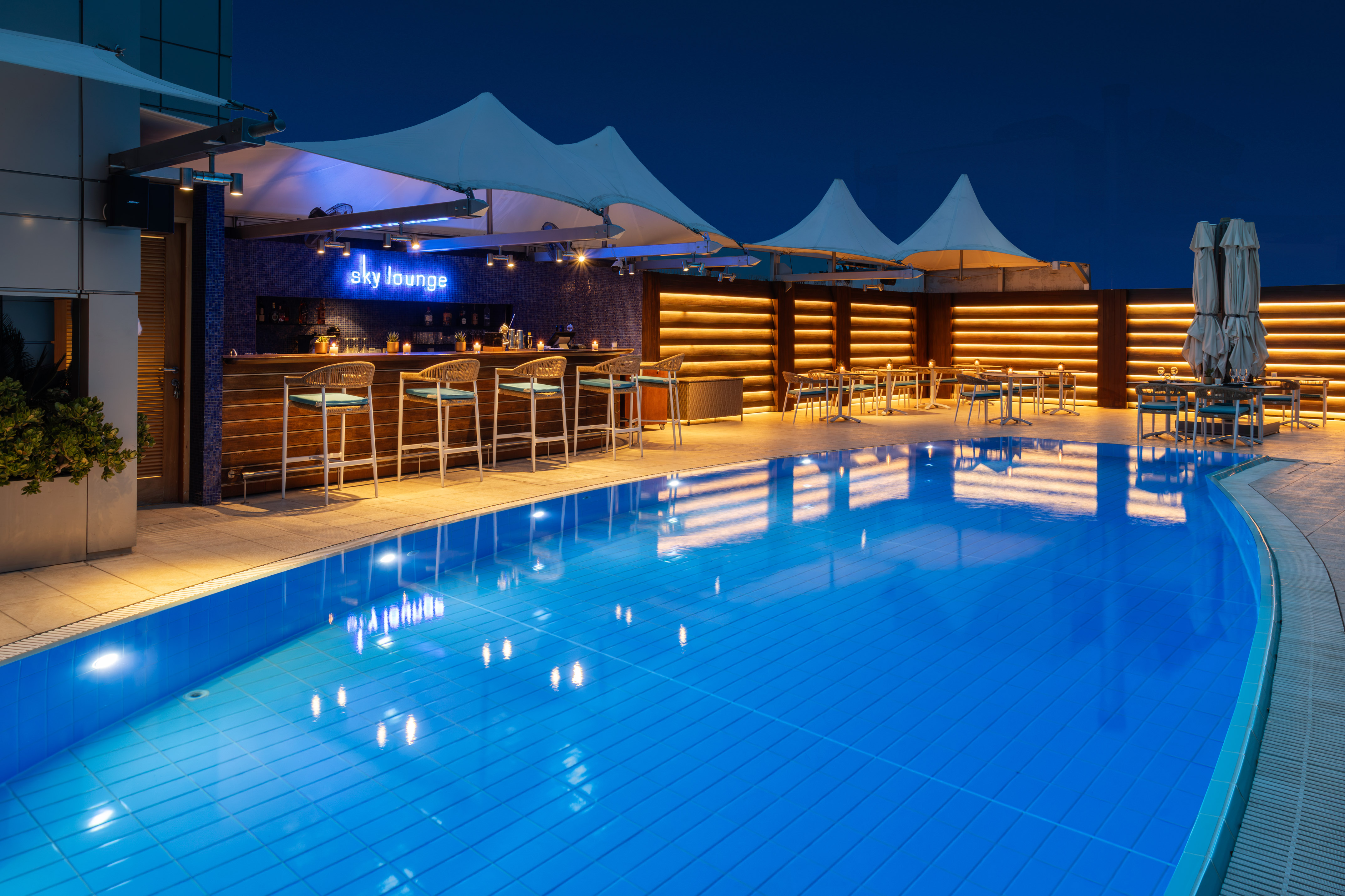 Rooftop Sky Lounge bar with illuminated pool and outdoor seating at night.
