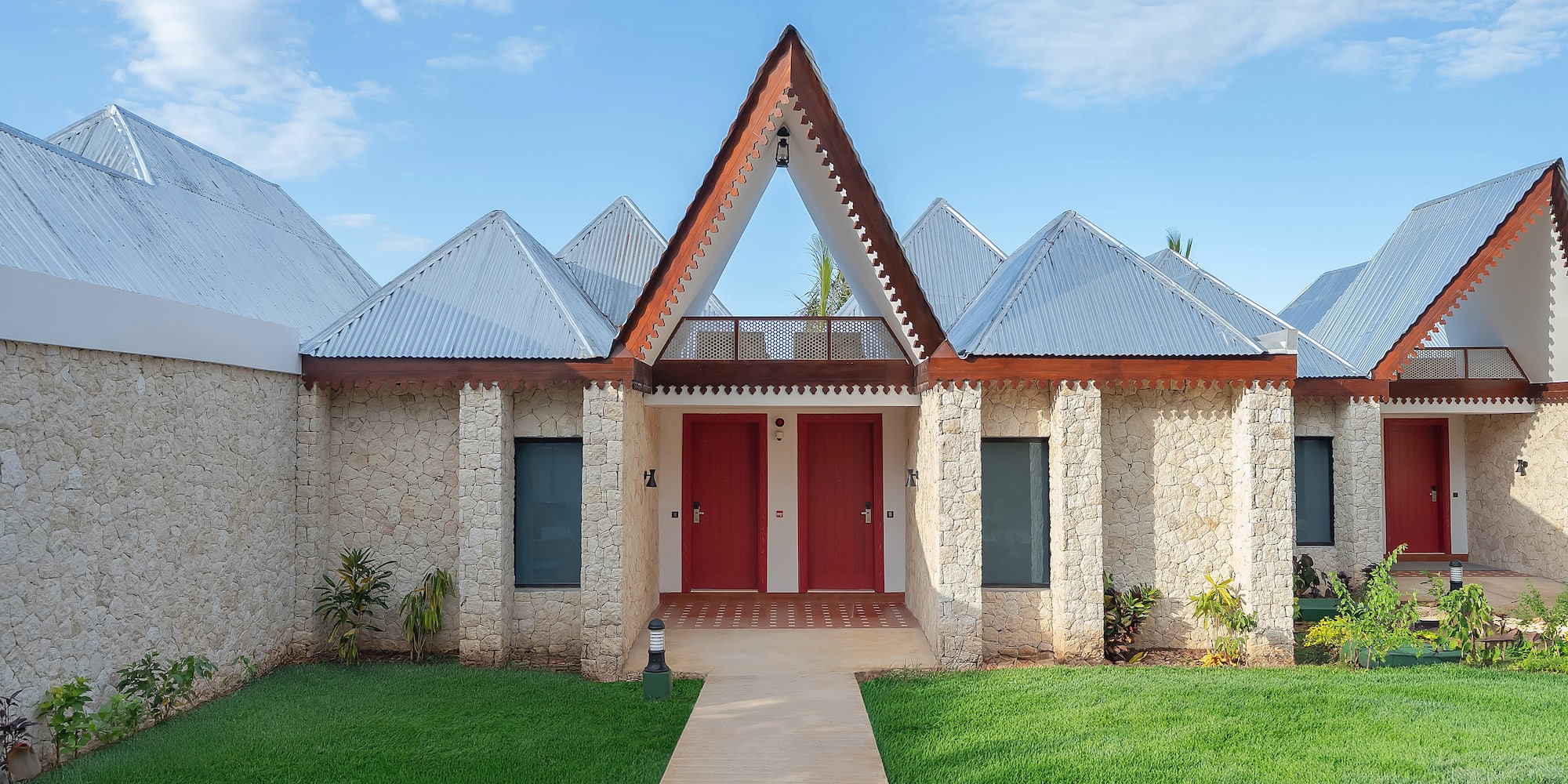 Stone tropical resort villas with peaked metal roofs, red doors, green lawn.